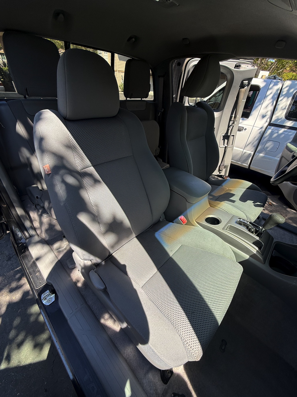 The interior of a vehicle showing the front seats, center console with cup holder, gear shift, and armrest, with a window view of another vehicle outside.