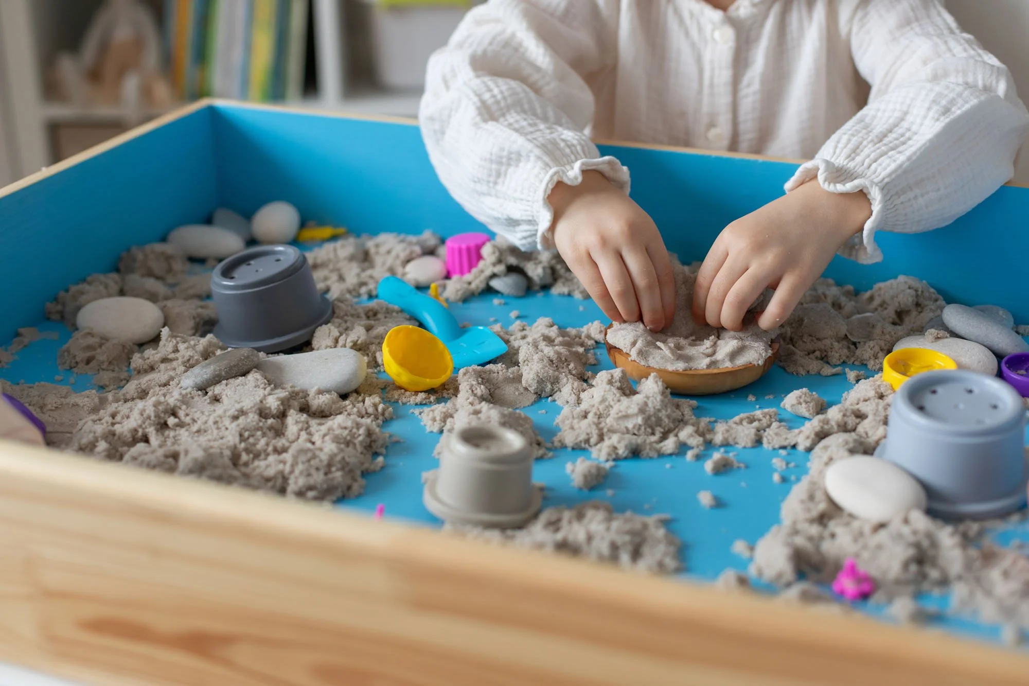 Child playing in a sandbox during a Play Therapy session with various sand toys such as shovels, buckets, and molds.