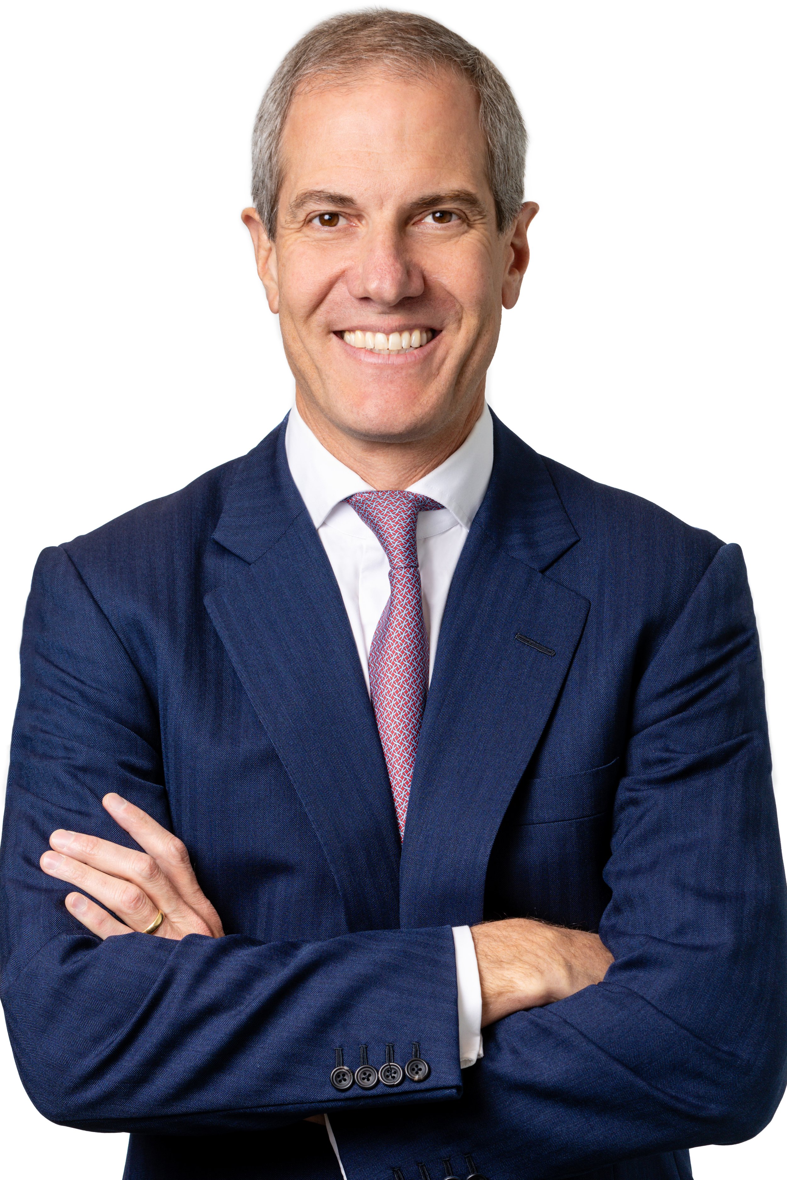 Professional man with gray hair, wearing a navy suit, white dress shirt, and red tie, smiling, with arms crossed.