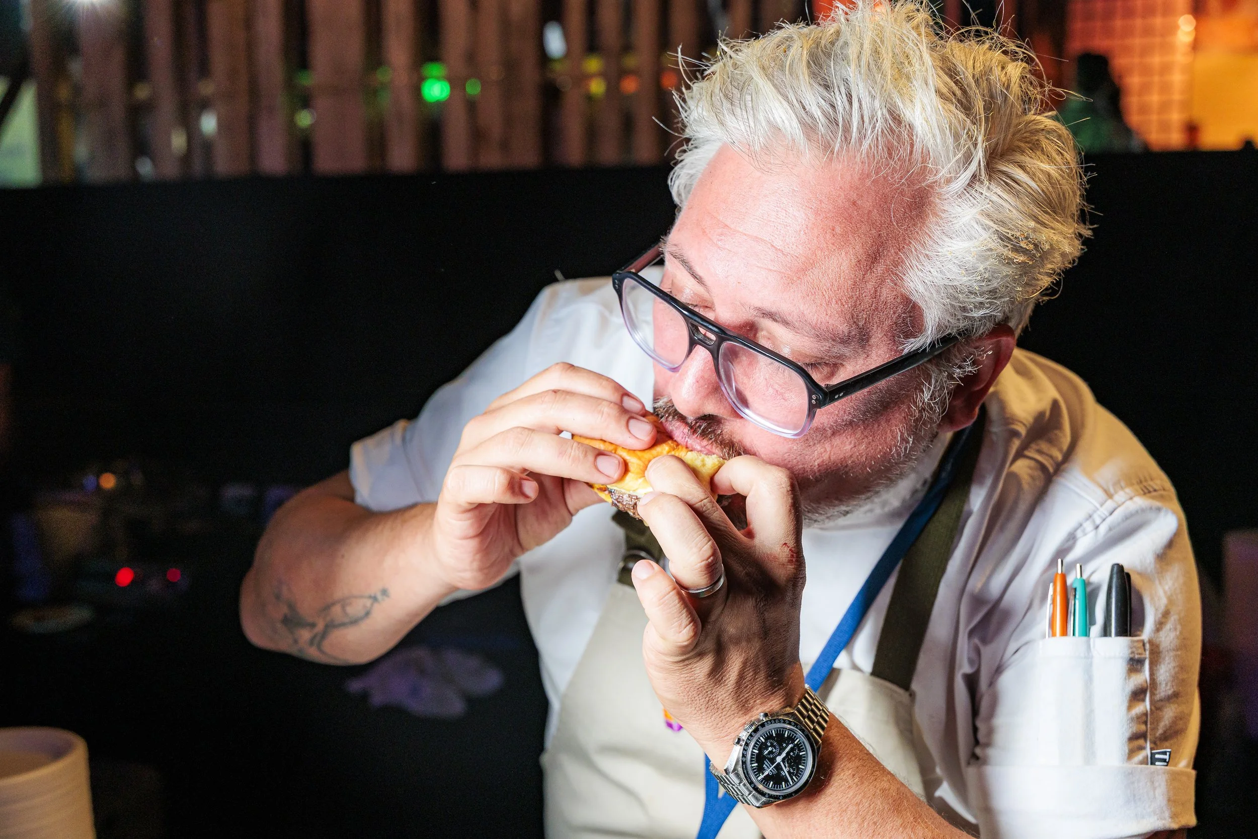 A chef in whites takes a bite of a slider at the Spoonfuls gala