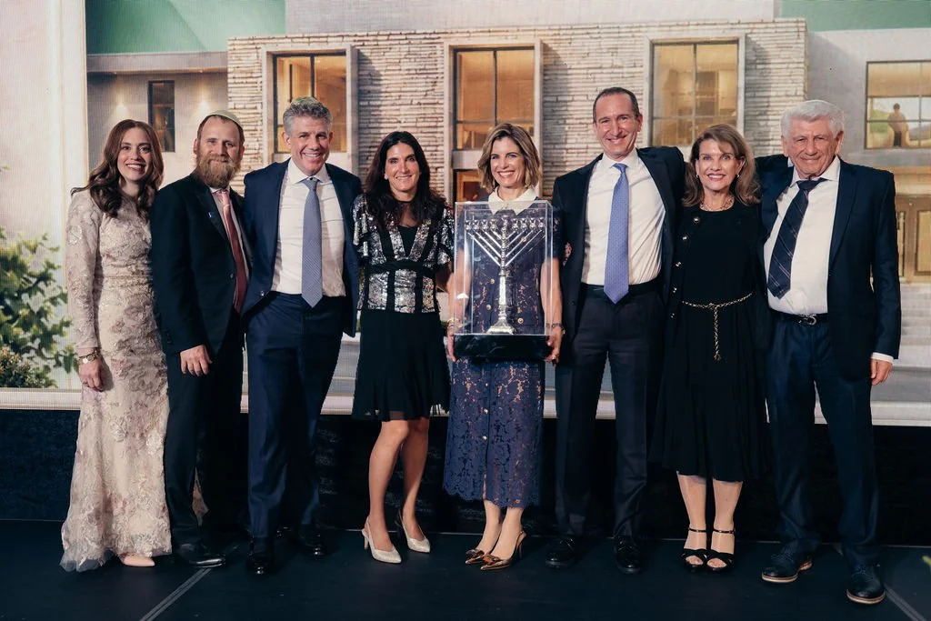 Eight honorees and family members pose on stage in front of the house-themed backdrop