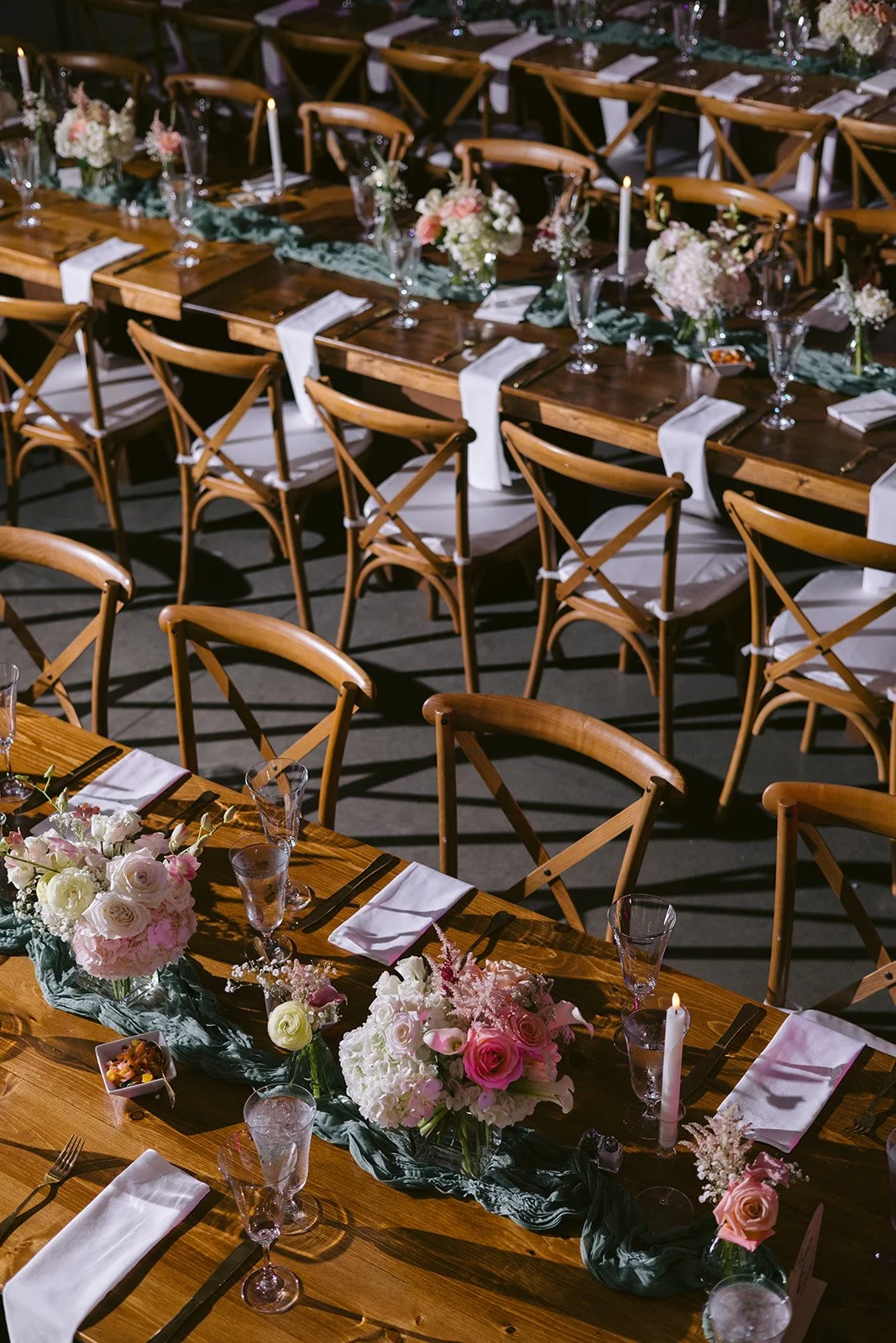 Overhead view of long wooden tables with pink floral runners and cross-back chairs at the art gallery wedding