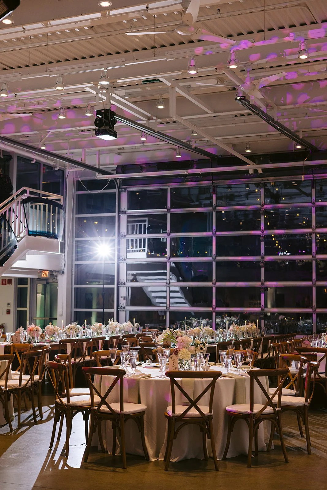 The reception space at night, with tables set beneath a wall of glass doors and pink uplighting
