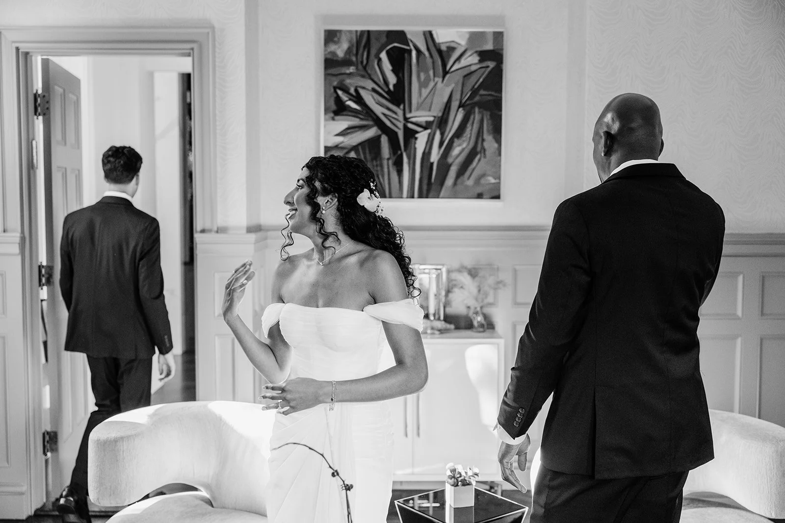 Black and white photo of the bride in a strapless gown turning toward a man in a suit in a living room
