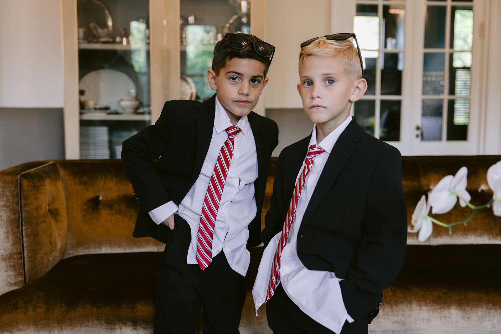 Two boys in suits and red striped ties pose in a living room before the wedding