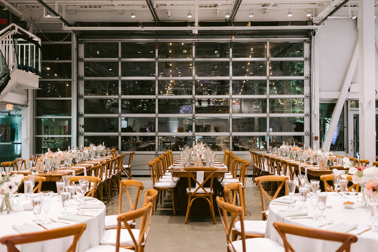 Dinner tables set in the gallery in front of a wall of glass garage doors