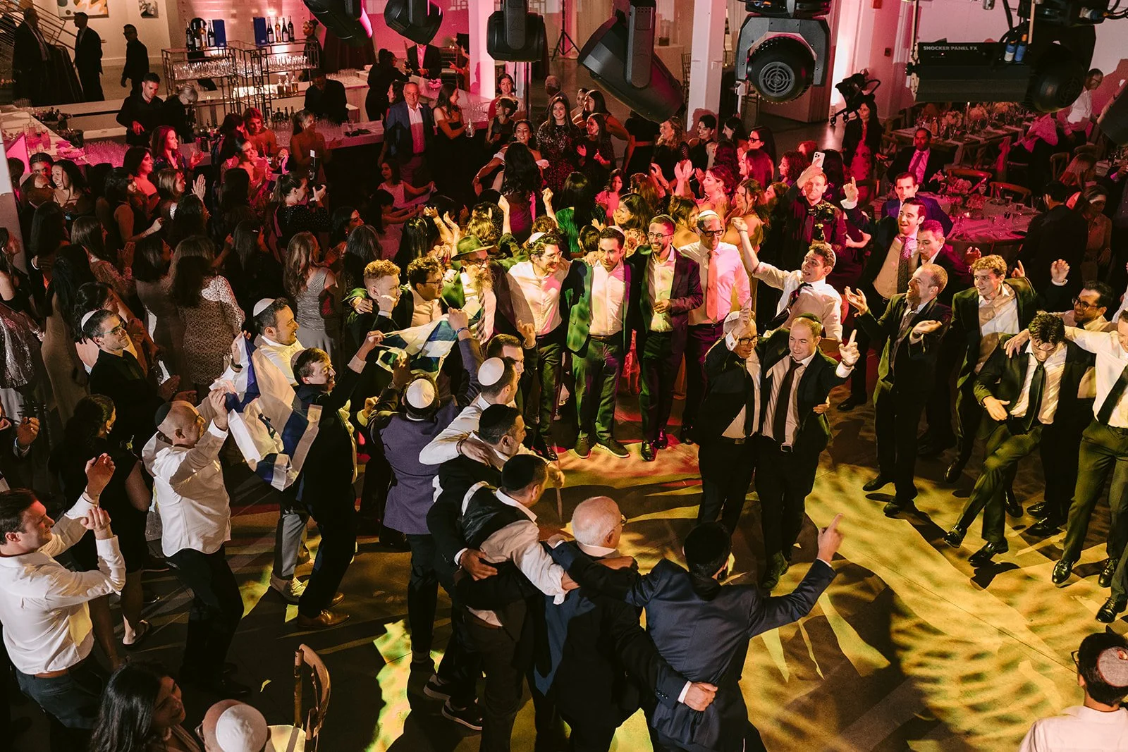 Guests dance arm in arm in a circle on a colorfully lit wedding dance floor