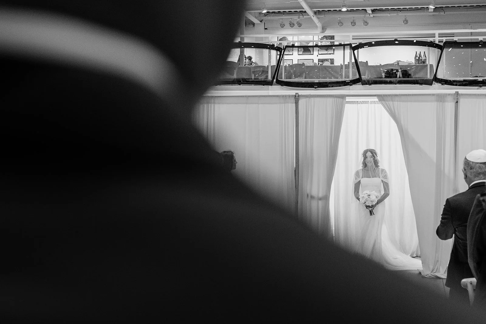 Black and white photo of the bride waiting behind a sheer curtain before the ceremony