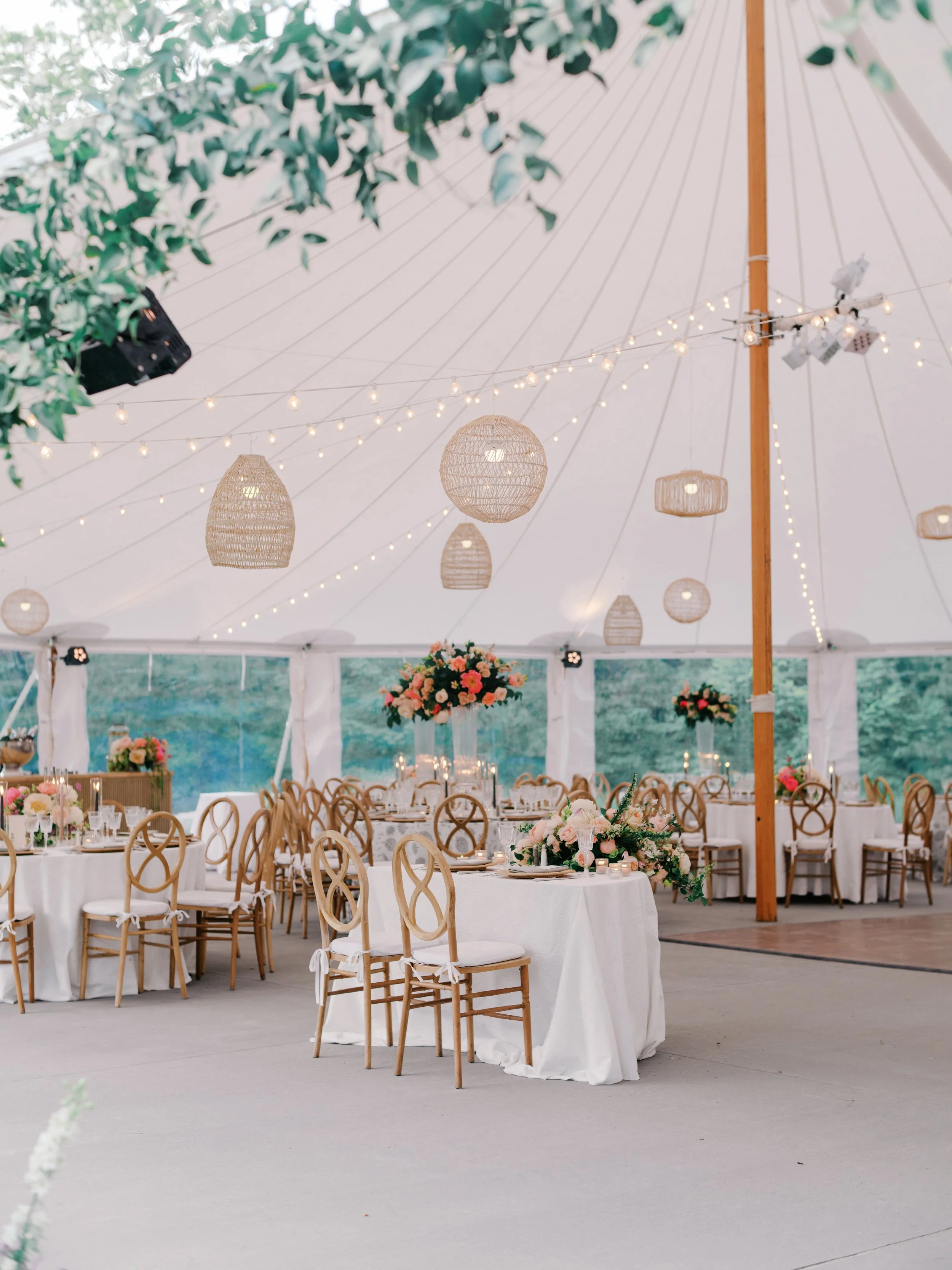 A sailcloth tent set with round tables, gold chairs, and hanging woven lanterns at deCordova Sculpture Park