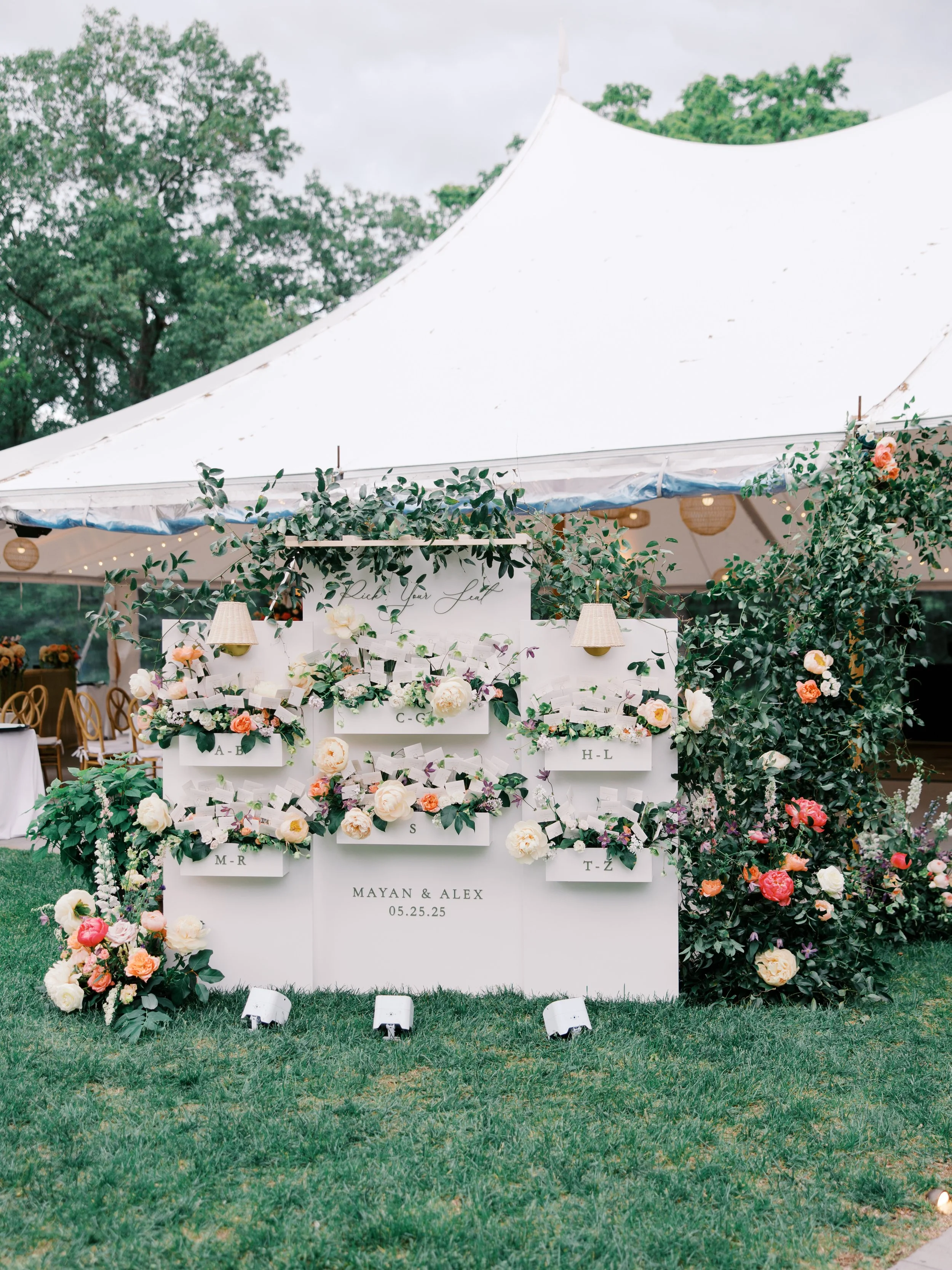 A white seating display for Mayan and Alex trimmed with flowers on the lawn outside the tent