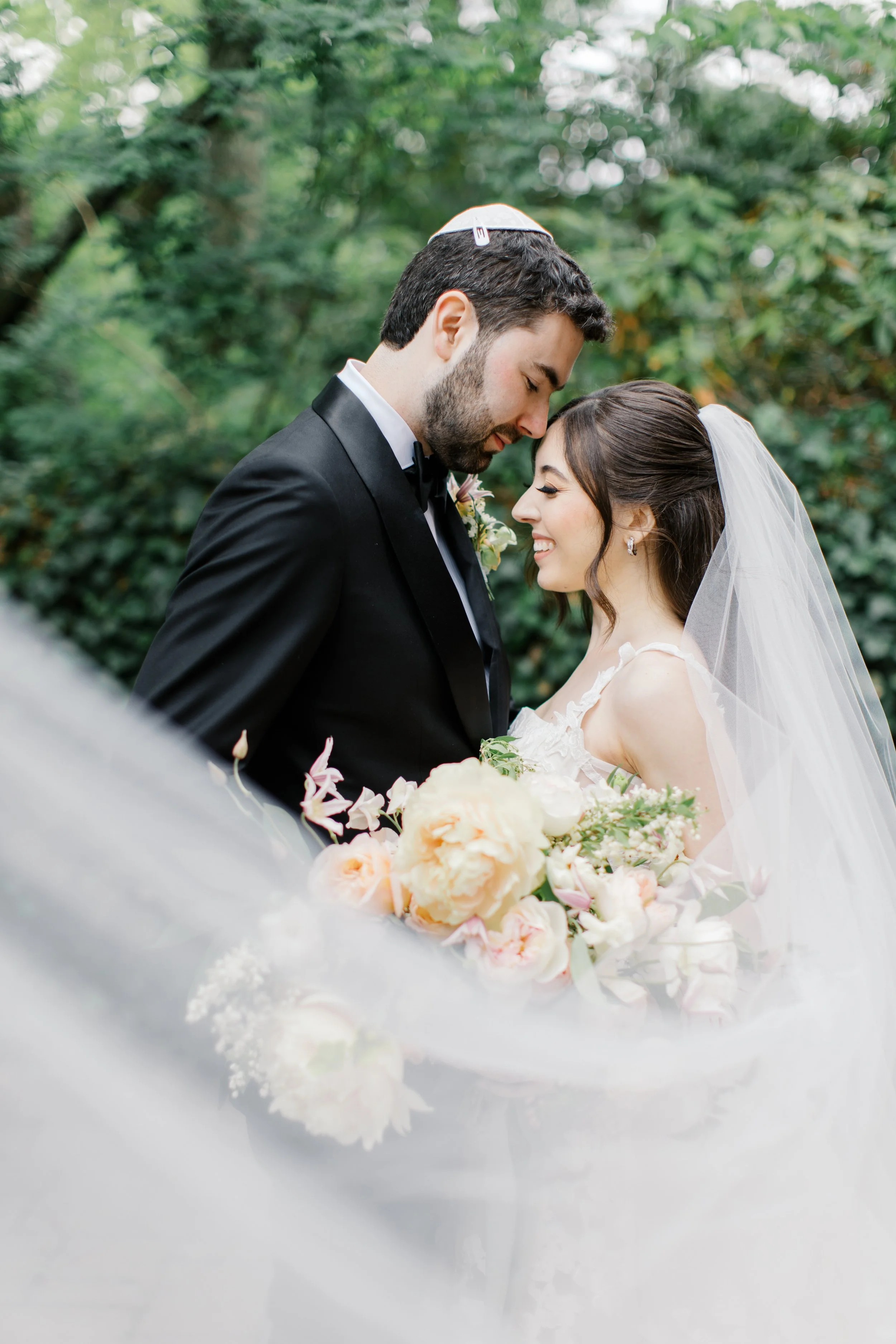 The bride and groom touch foreheads as her veil sweeps across the frame
