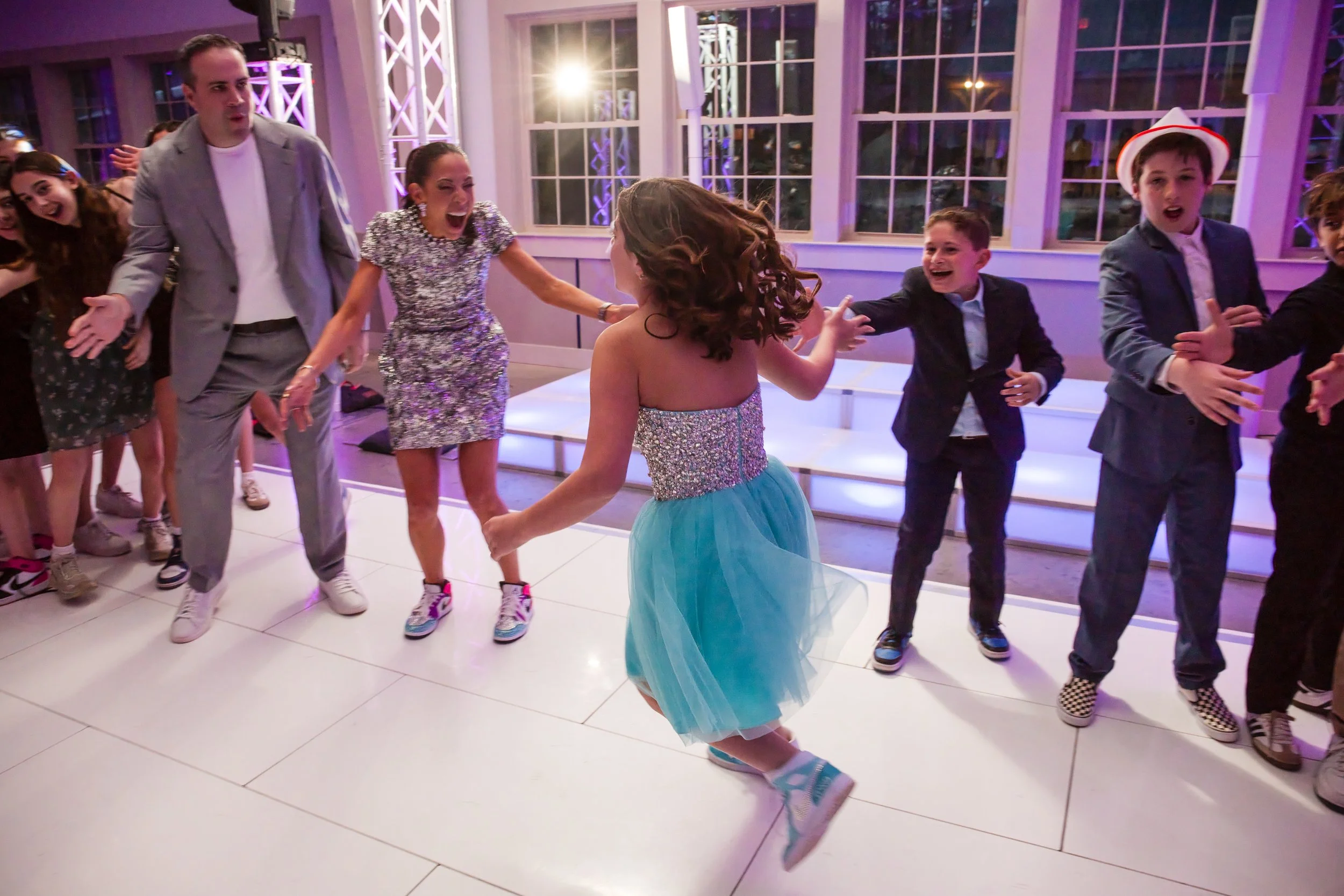 The bat mitzvah girl in a teal tulle dress dances with a guest on a white dance floor at Camp Ramah