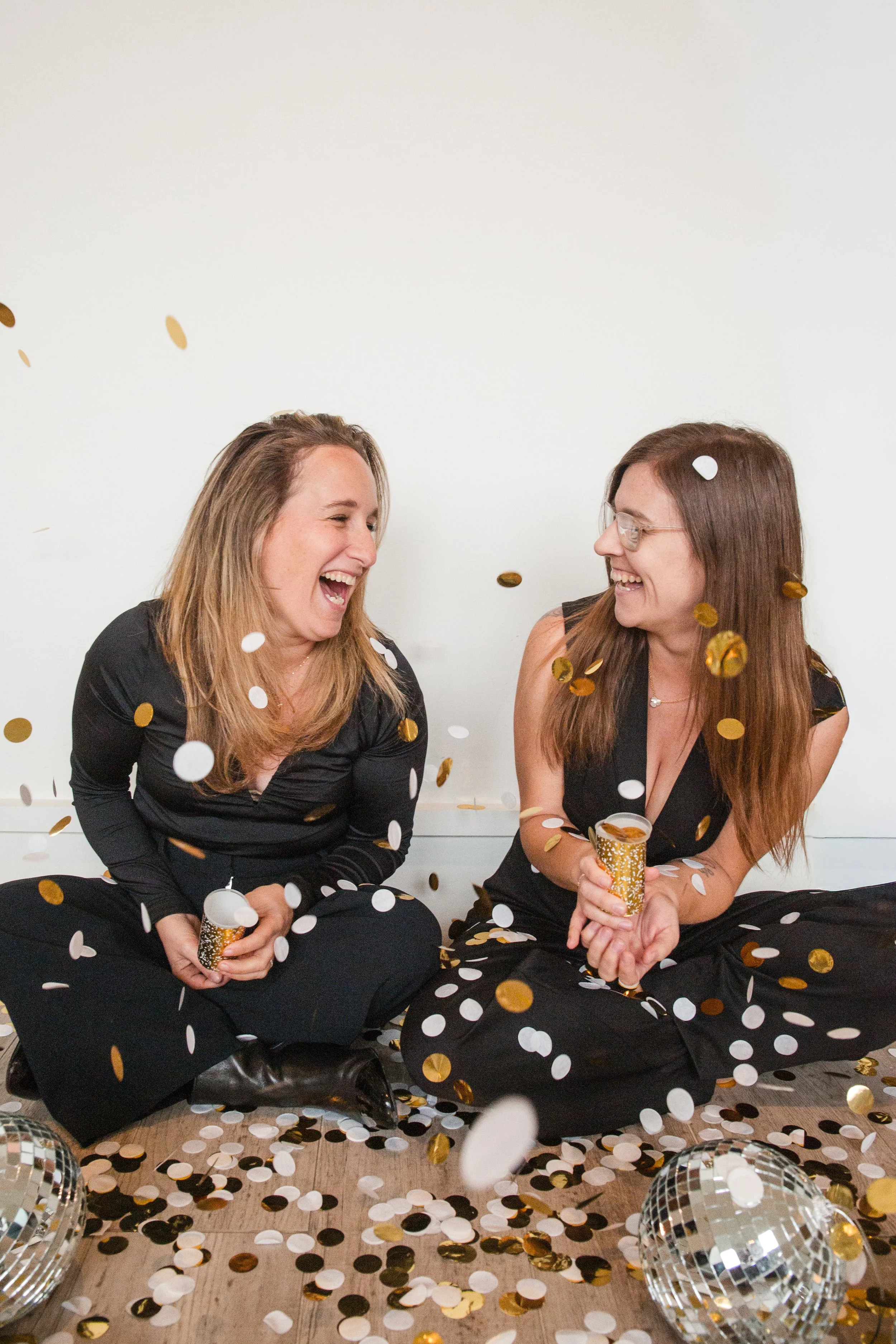 Leora and Mel of the ONE28 team laughing together surrounded by confetti