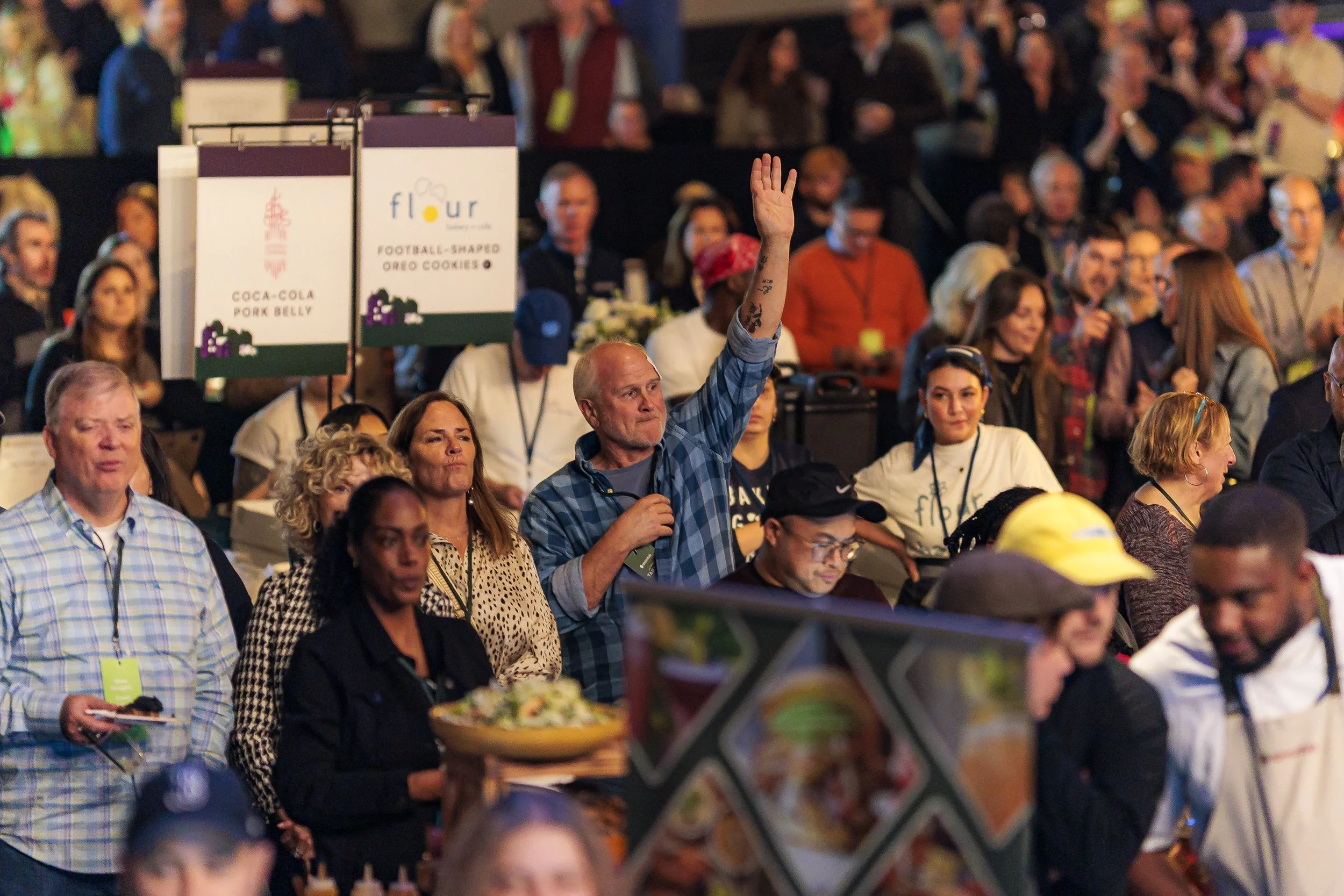 Auction item signs are held up over a cheering crowd during the Spoonfuls gala auction