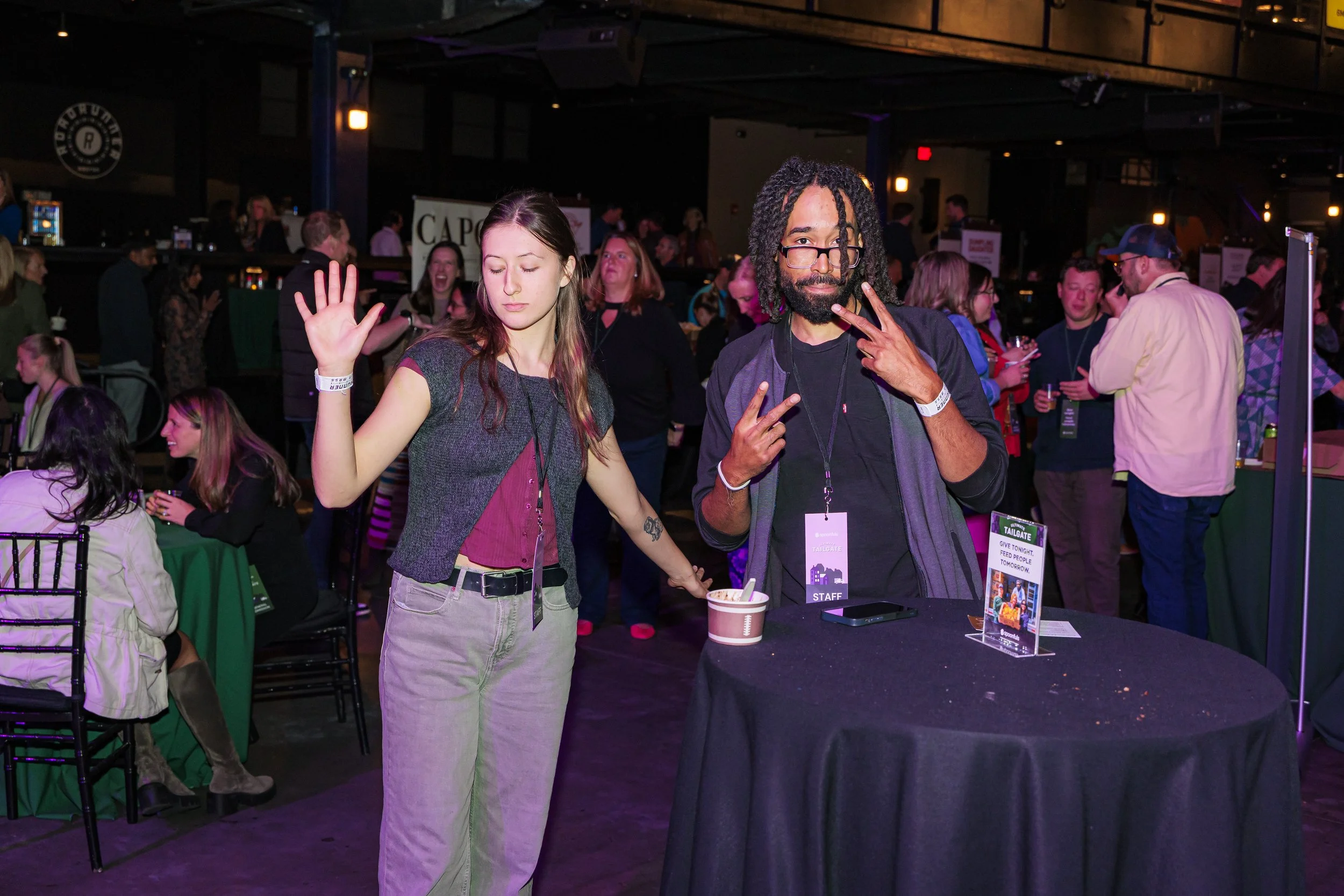 Guests wave and pose by a cocktail table in the crowd at the Spoonfuls Ultimate Tailgate
