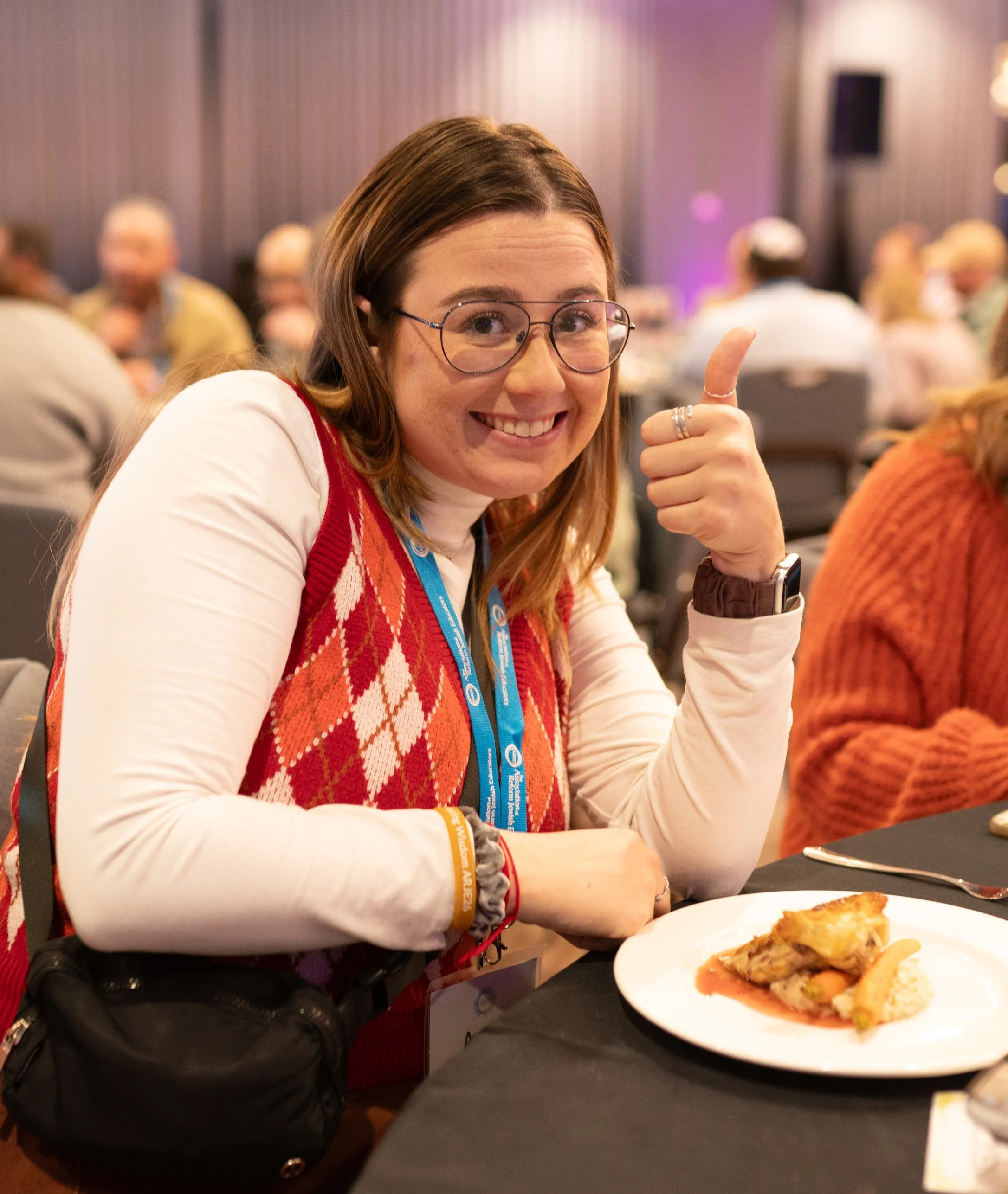 A smiling attendee gives a thumbs-up at her table during a meal at the ARJE conference