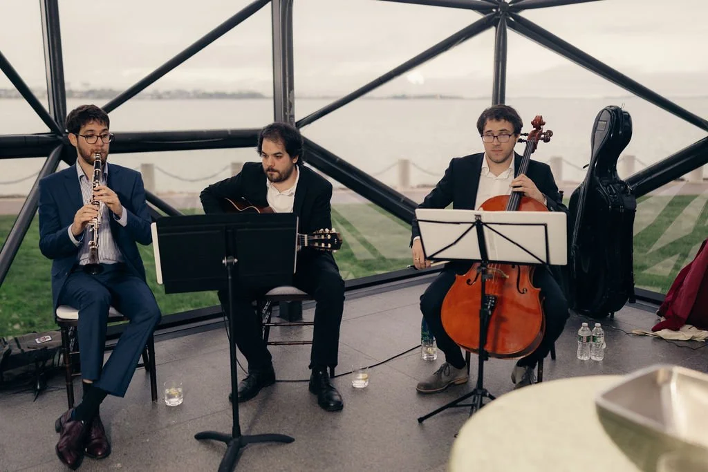 A trio of clarinet, guitar, and cello plays before floor-to-ceiling windows during the cocktail hour