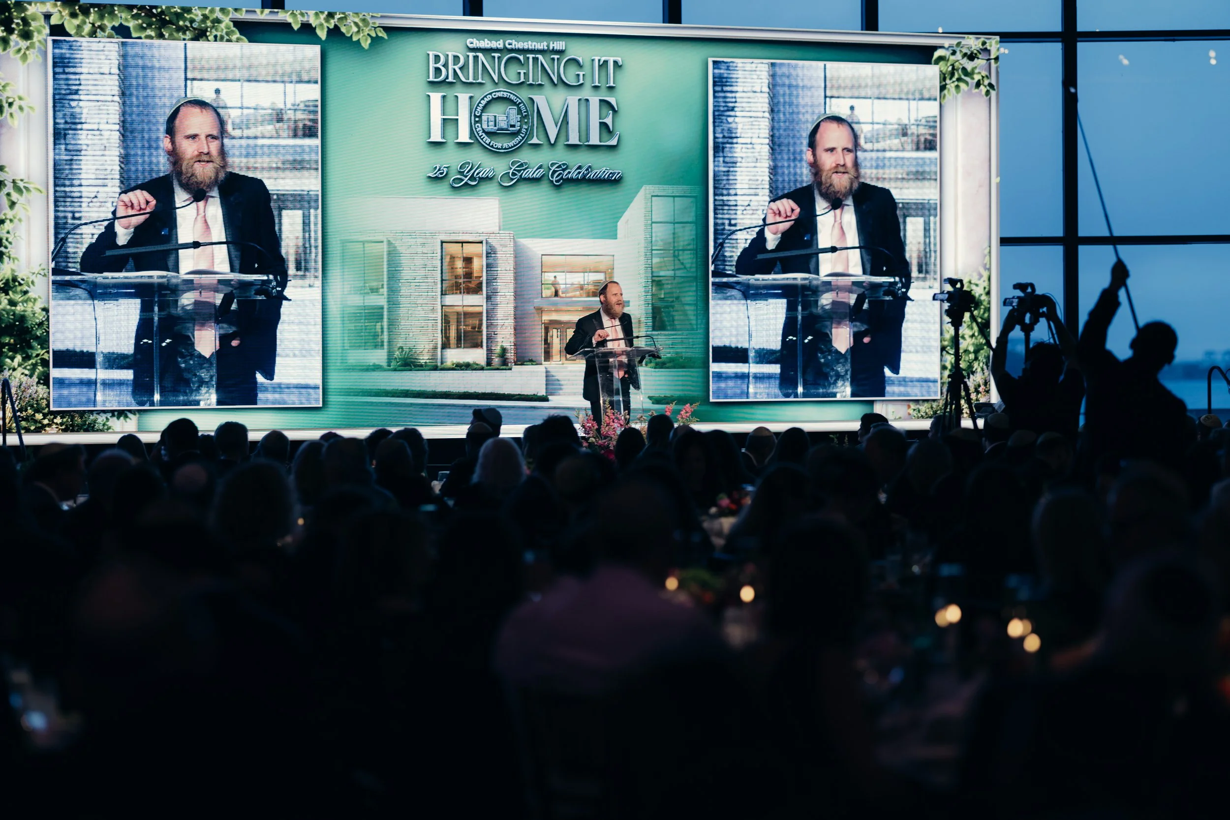 Speaker addressing the crowd beneath a Bringing It Home event screen