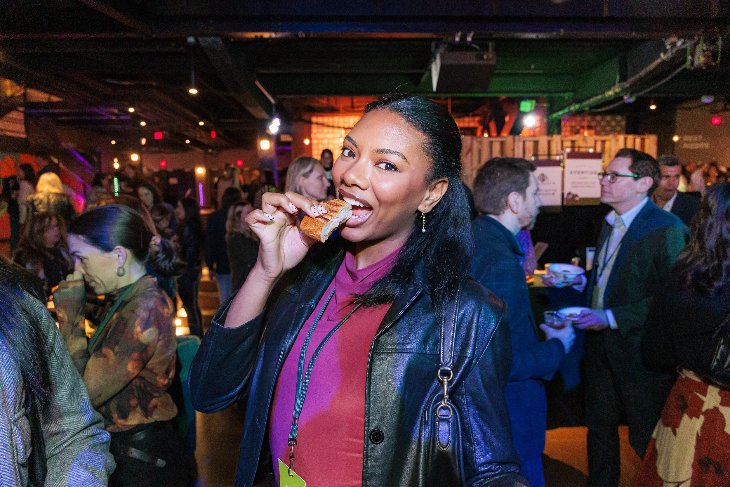 A smiling guest samples a bite in the crowded venue at the Spoonfuls Ultimate Tailgate