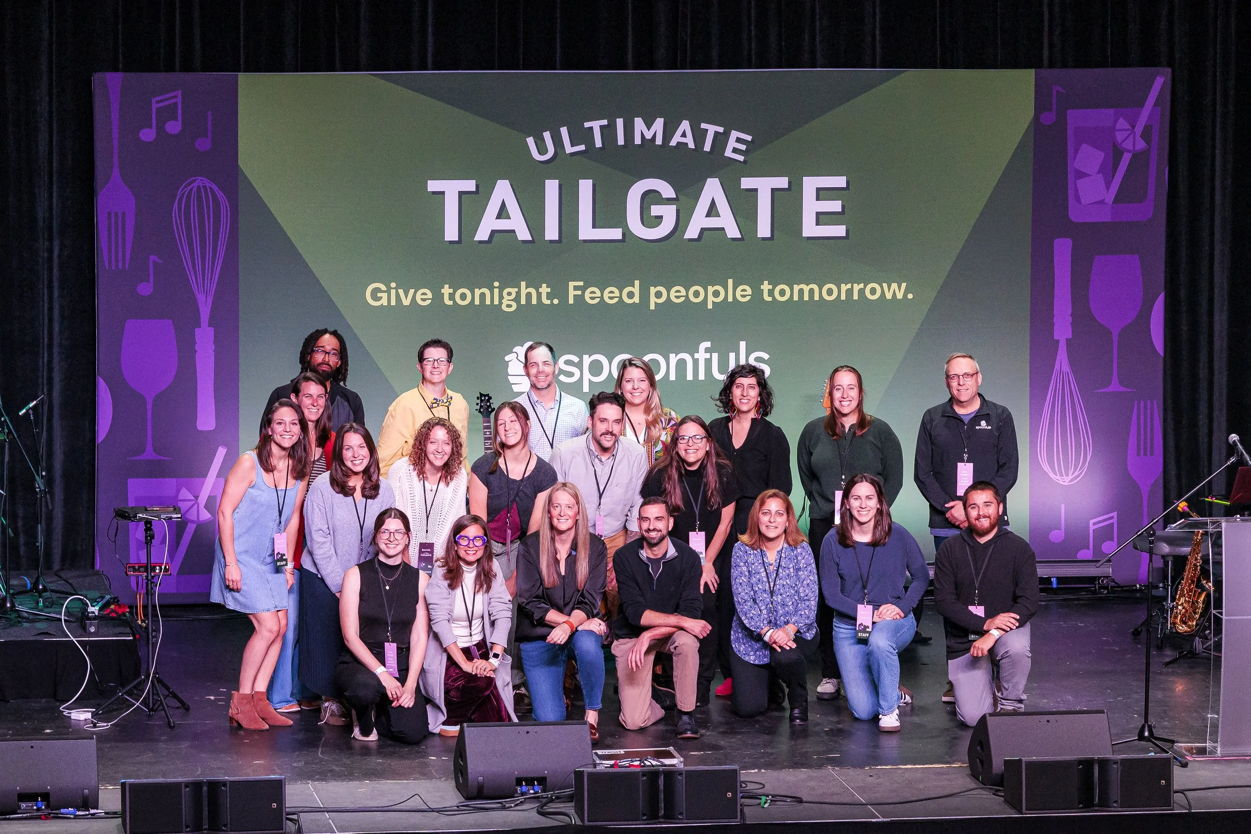 The Spoonfuls team poses on stage in front of the Ultimate Tailgate backdrop reading Give tonight. Feed people tomorrow.