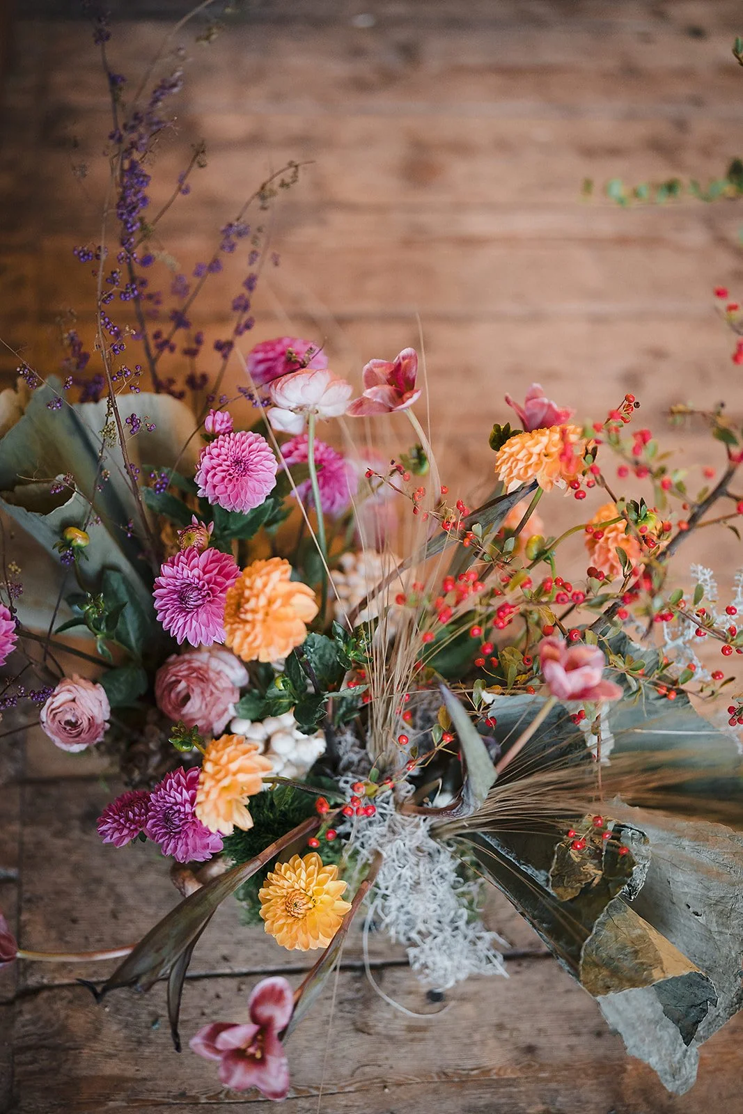 A lush floral installation of dahlias and dried leaves against a weathered wood wall