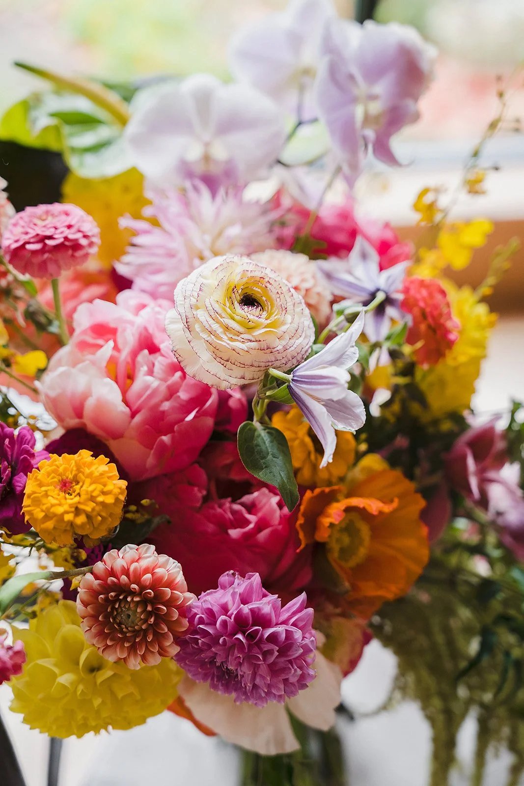Close-up of a bright arrangement of peonies, ranunculus, dahlias, and orchids