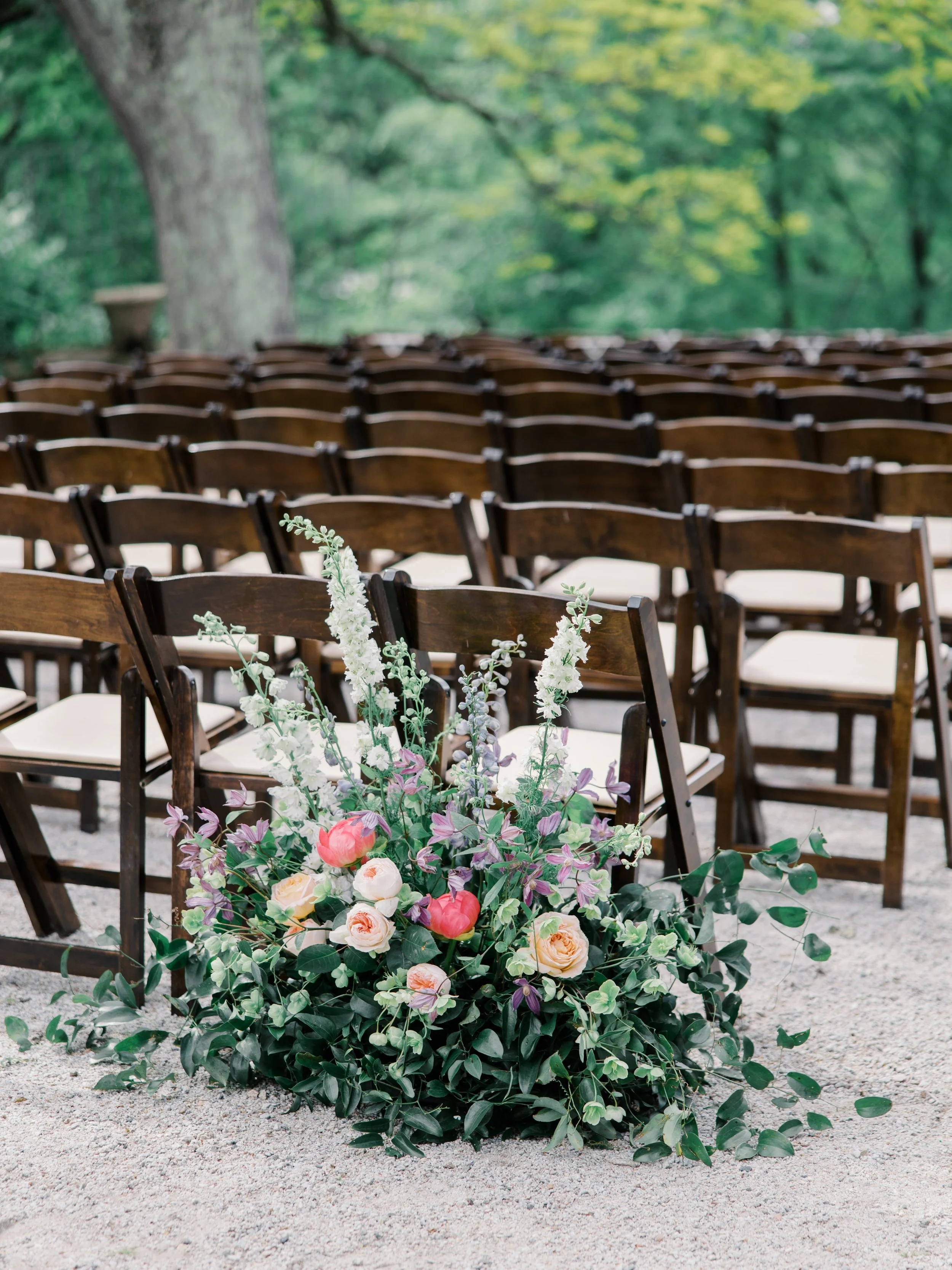 A low floral arrangement marks the end of a row of wooden ceremony chairs