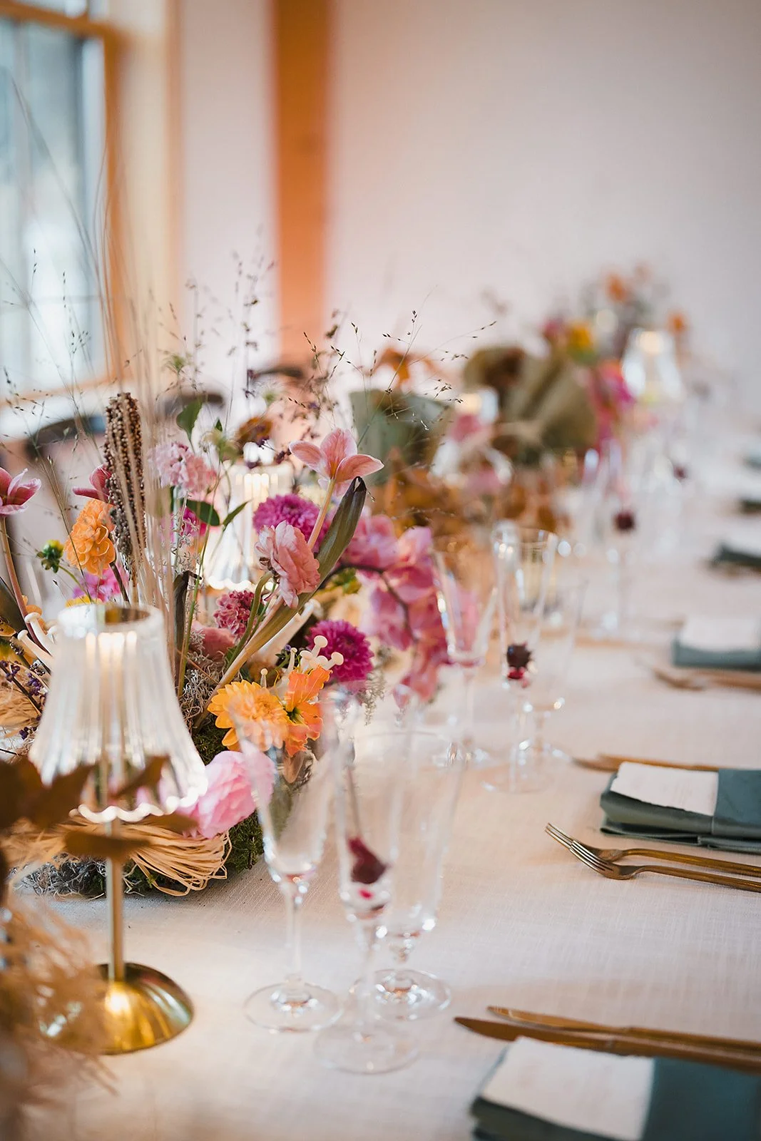 Dried grasses, pink blooms, and glass lamps line a long reception table