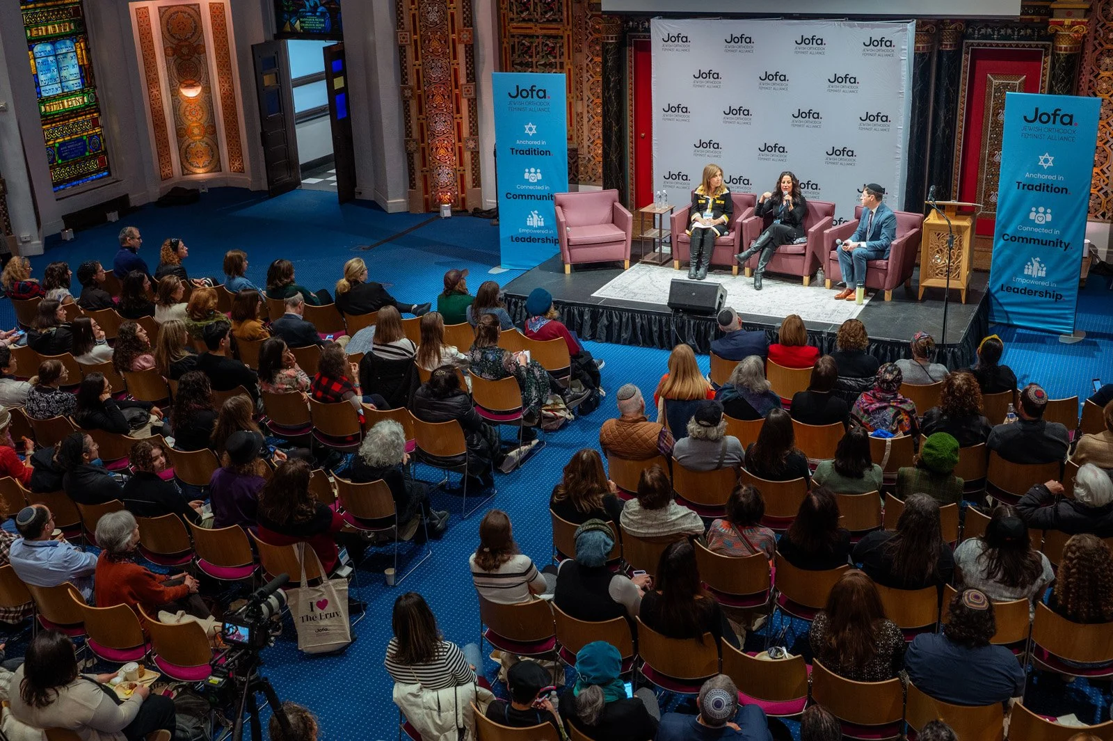 An audience fills the sanctuary for a panel discussion on a blue-carpeted stage at the JOFA conference