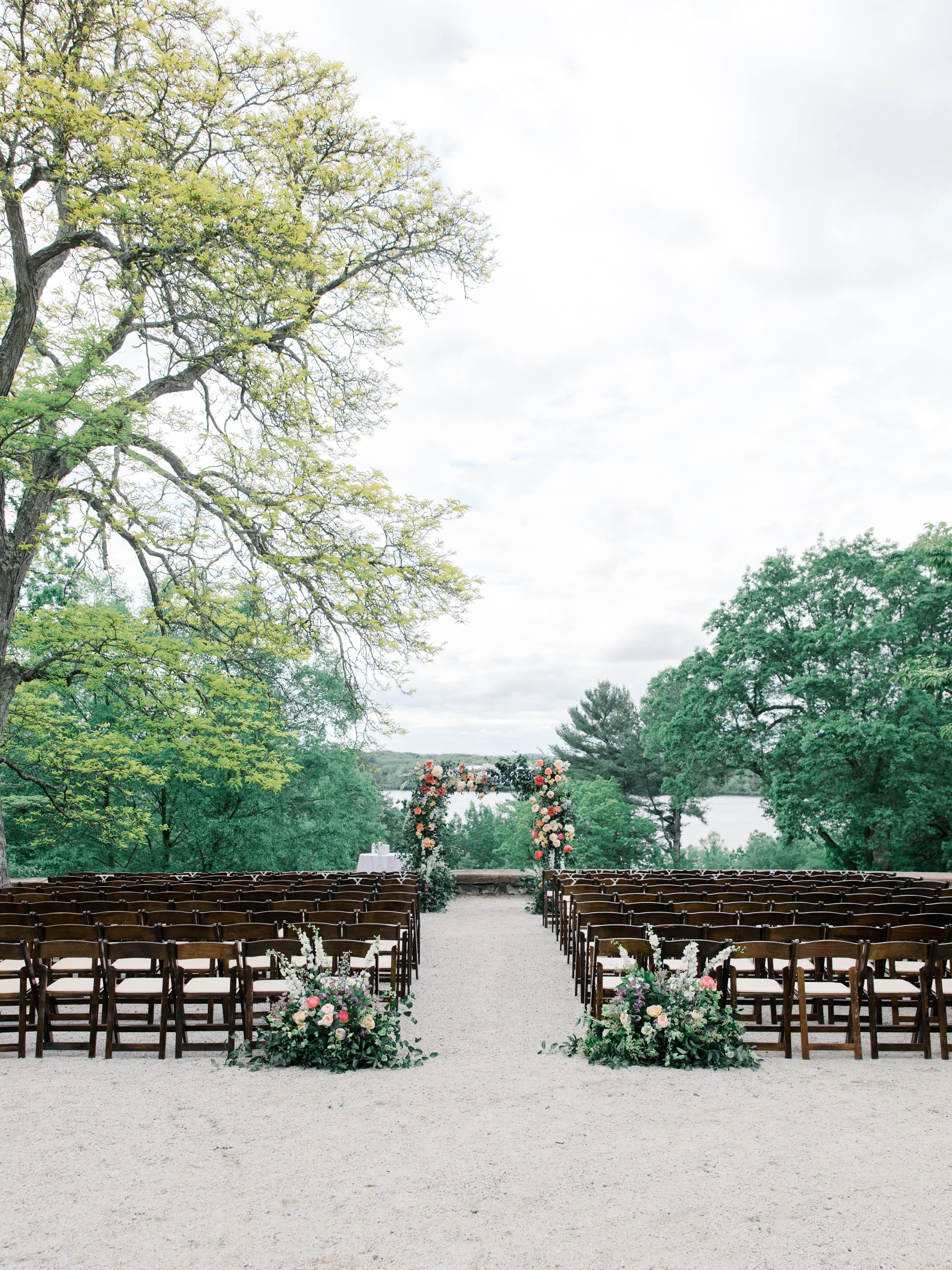 Rows of wooden ceremony chairs face a floral arch overlooking the treetops and pond