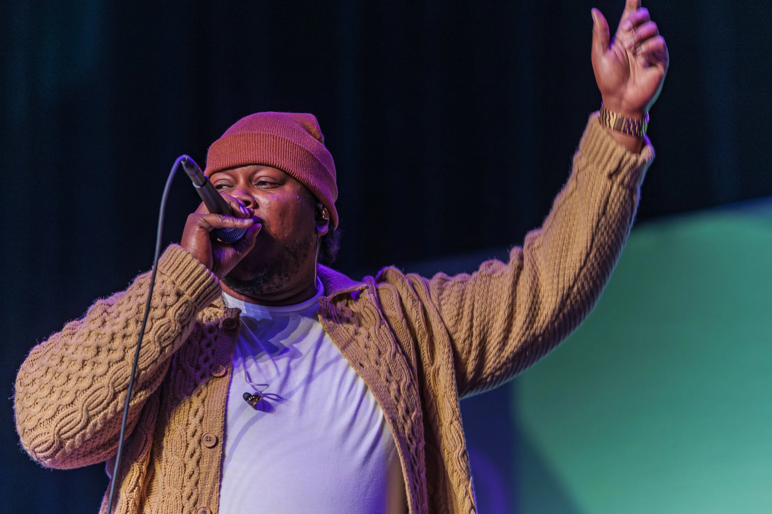 A performer in a knit cap sings into a microphone with one arm raised at the Spoonfuls gala