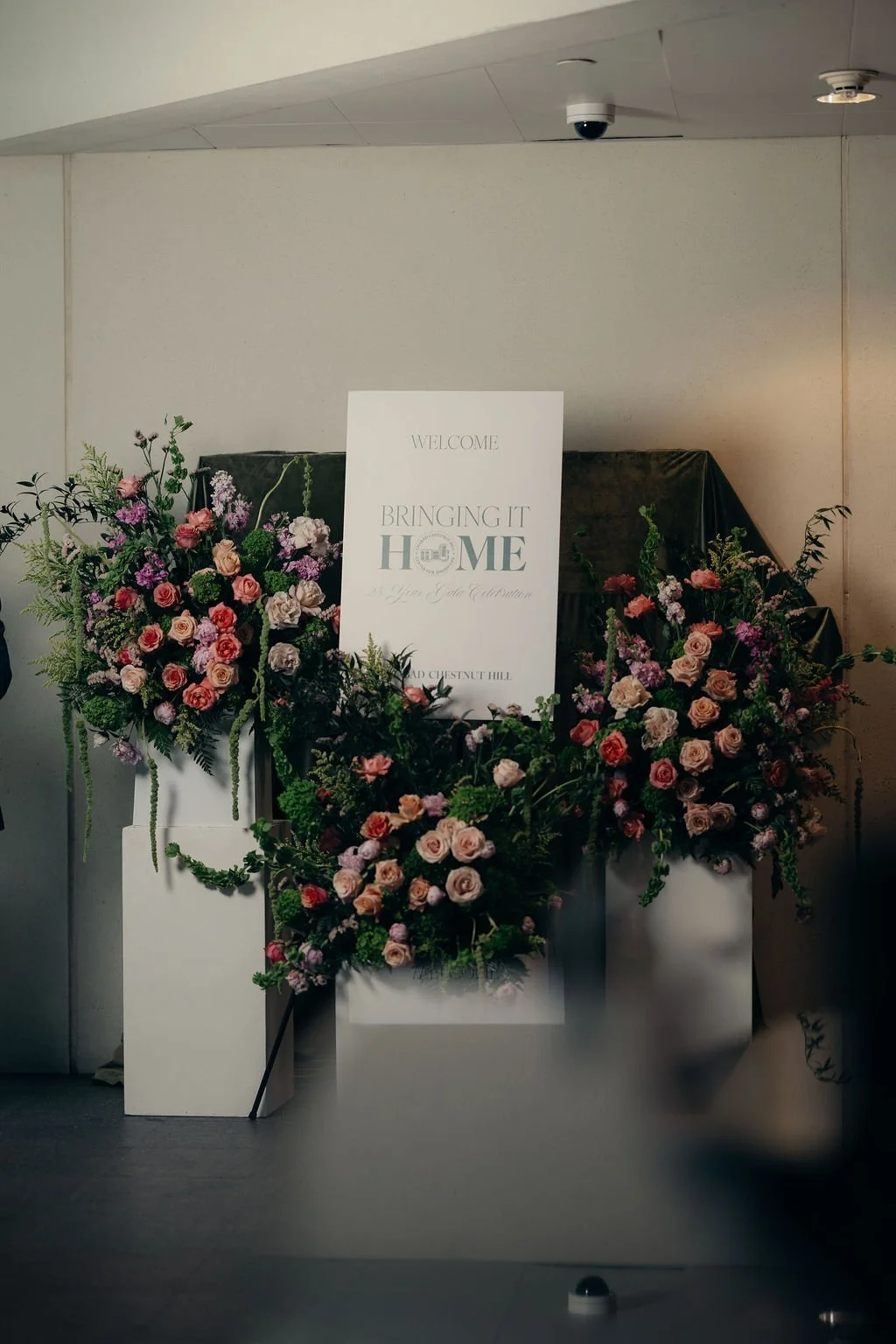A Bringing It Home welcome sign framed by pink and peach floral arrangements