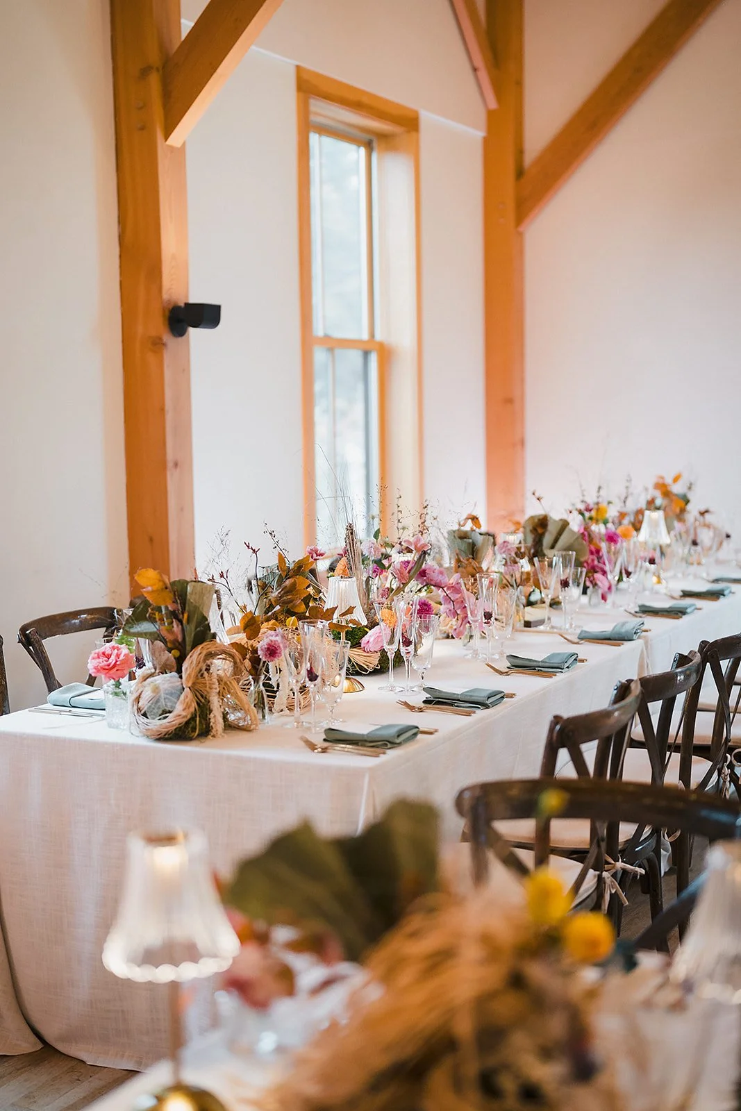 A long reception table with florals and glass lamps in a timber-framed room