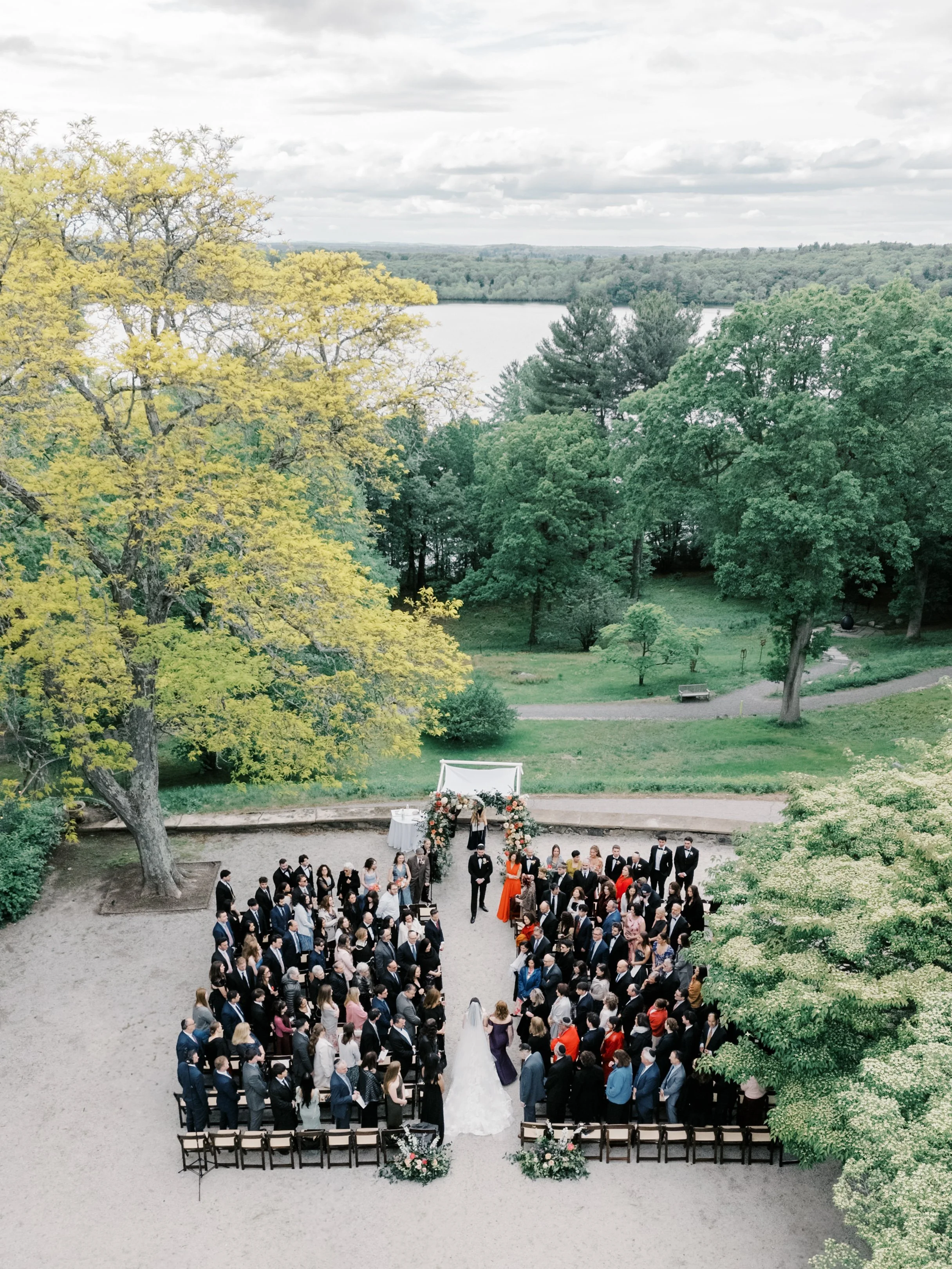 Aerial view of guests seated for the outdoor ceremony on a terrace above the pond