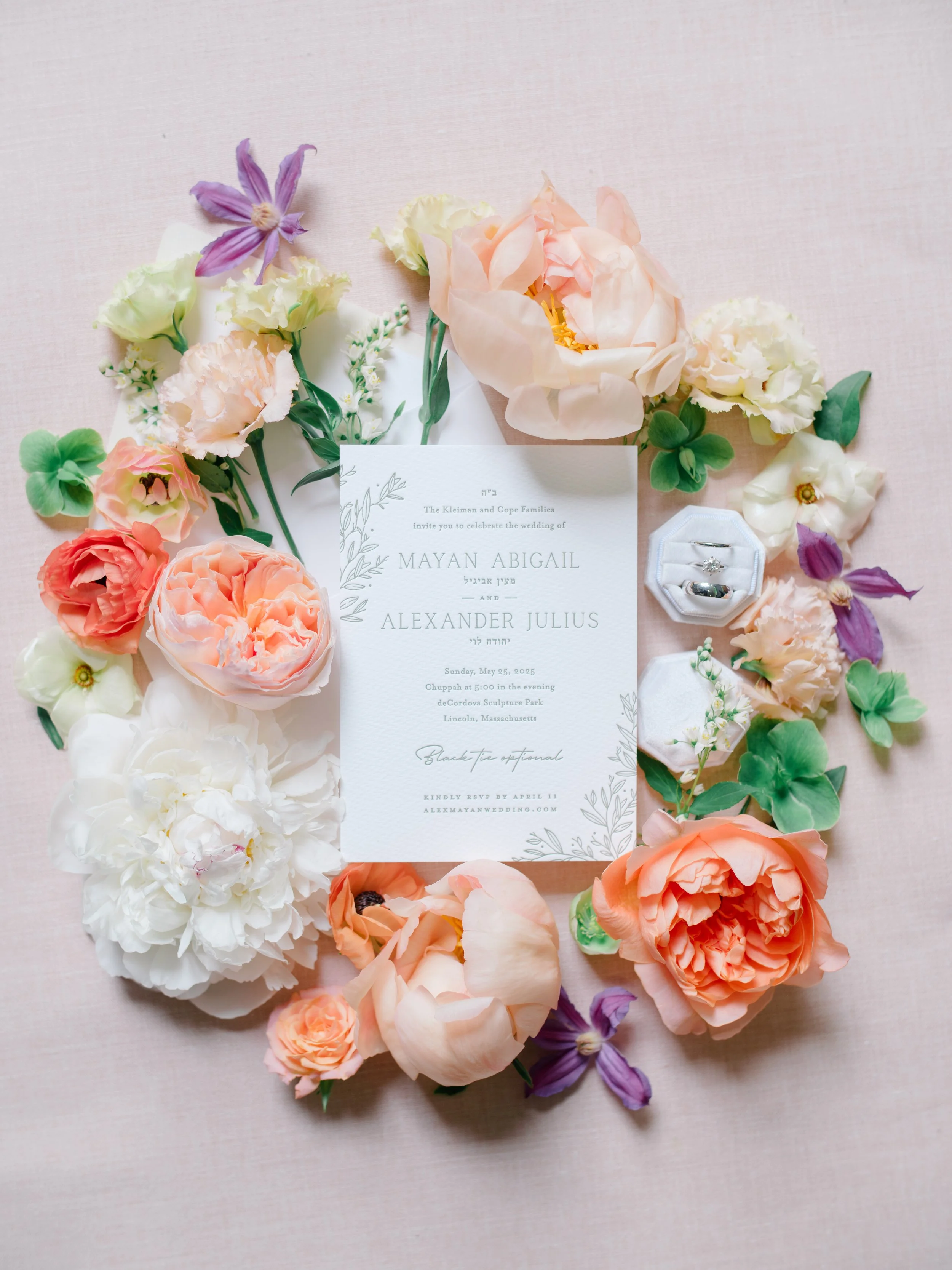 The wedding invitation framed by a ring of garden roses, peonies, and clematis