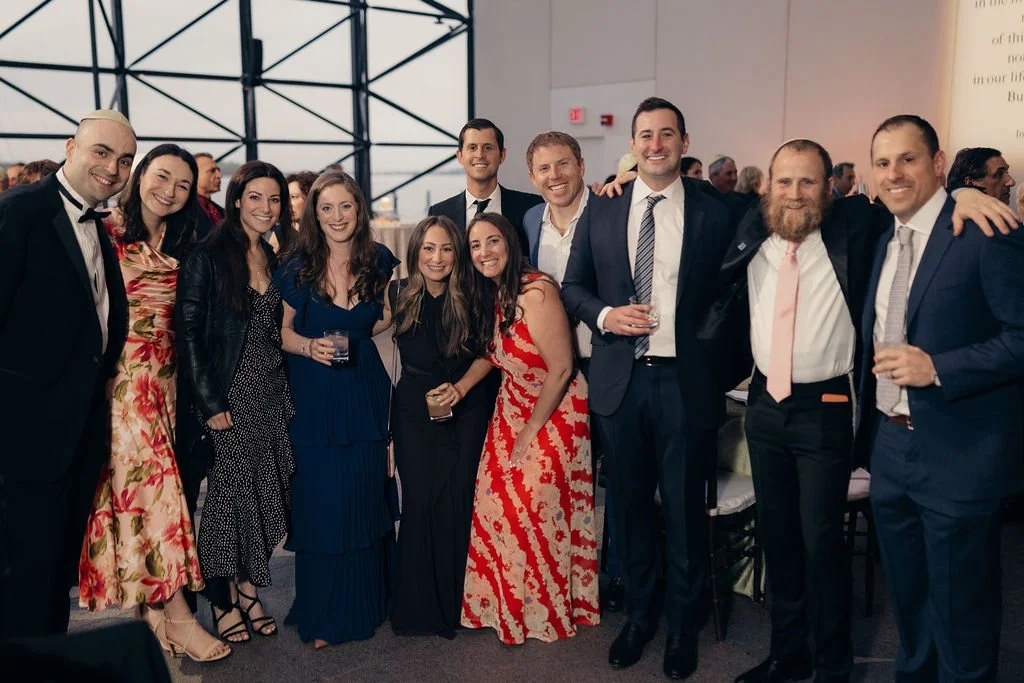 A group of guests in formal attire poses together beneath a glass ceiling at the Chabad Chestnut Hill gala