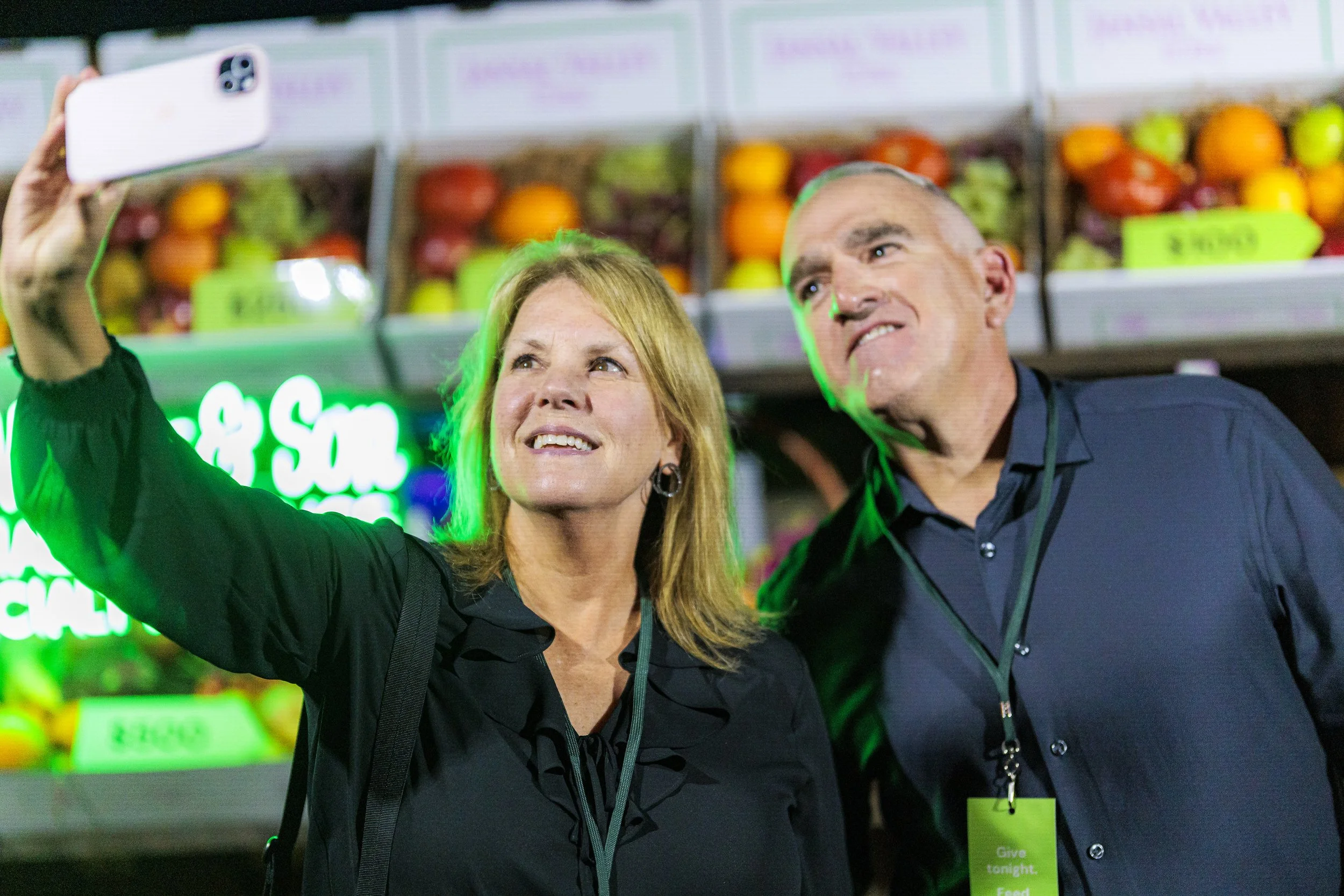 Two guests take a selfie in front of the specialty produce wall at the Spoonfuls gala