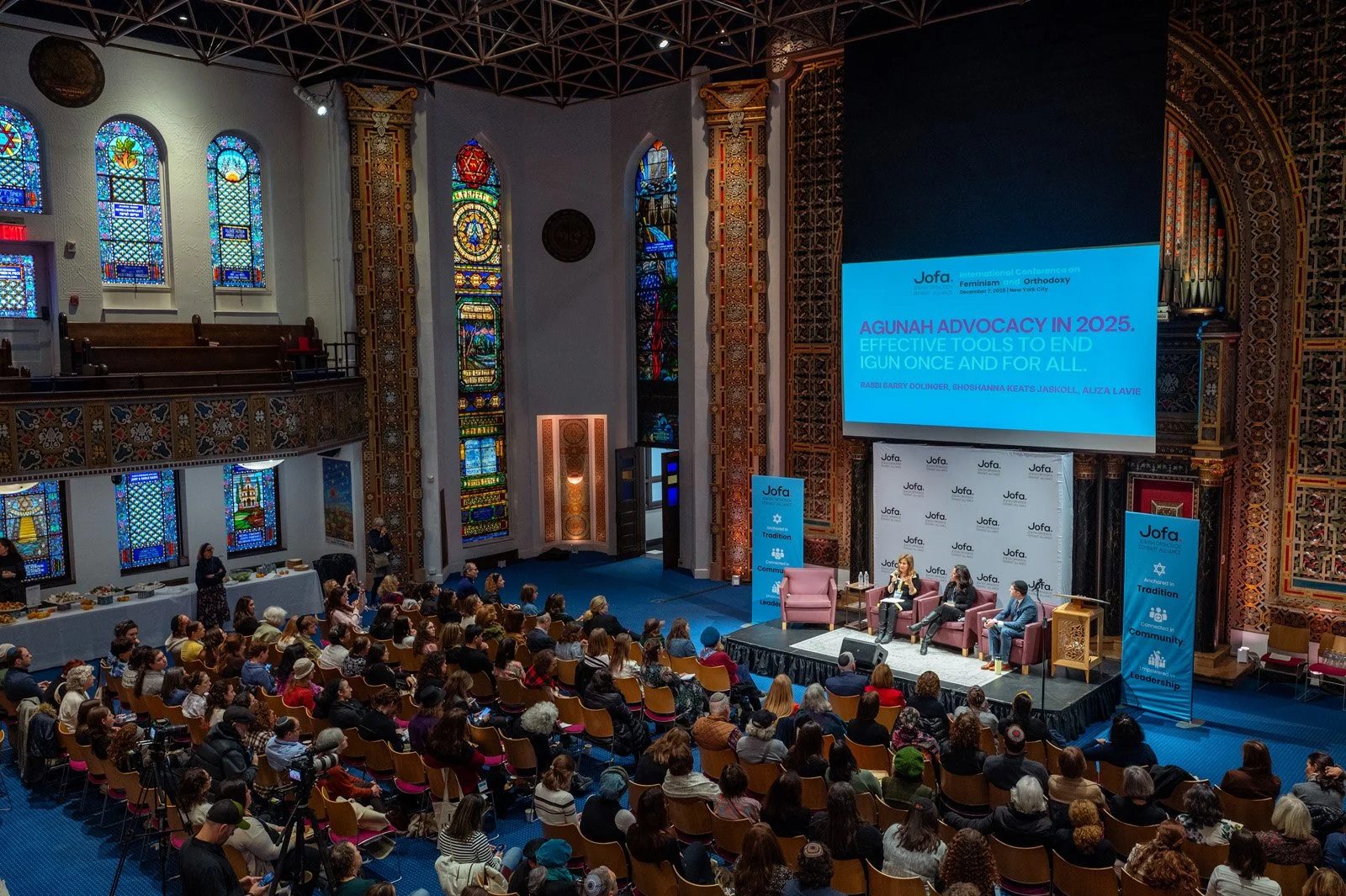 A full sanctuary beneath stained glass windows watches a panel on agunah advocacy at the JOFA International Conference in New York