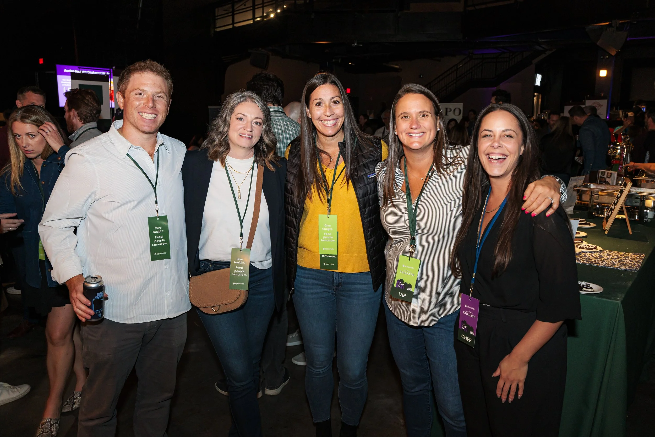 Five guests with event lanyards pose together at the Spoonfuls Ultimate Tailgate