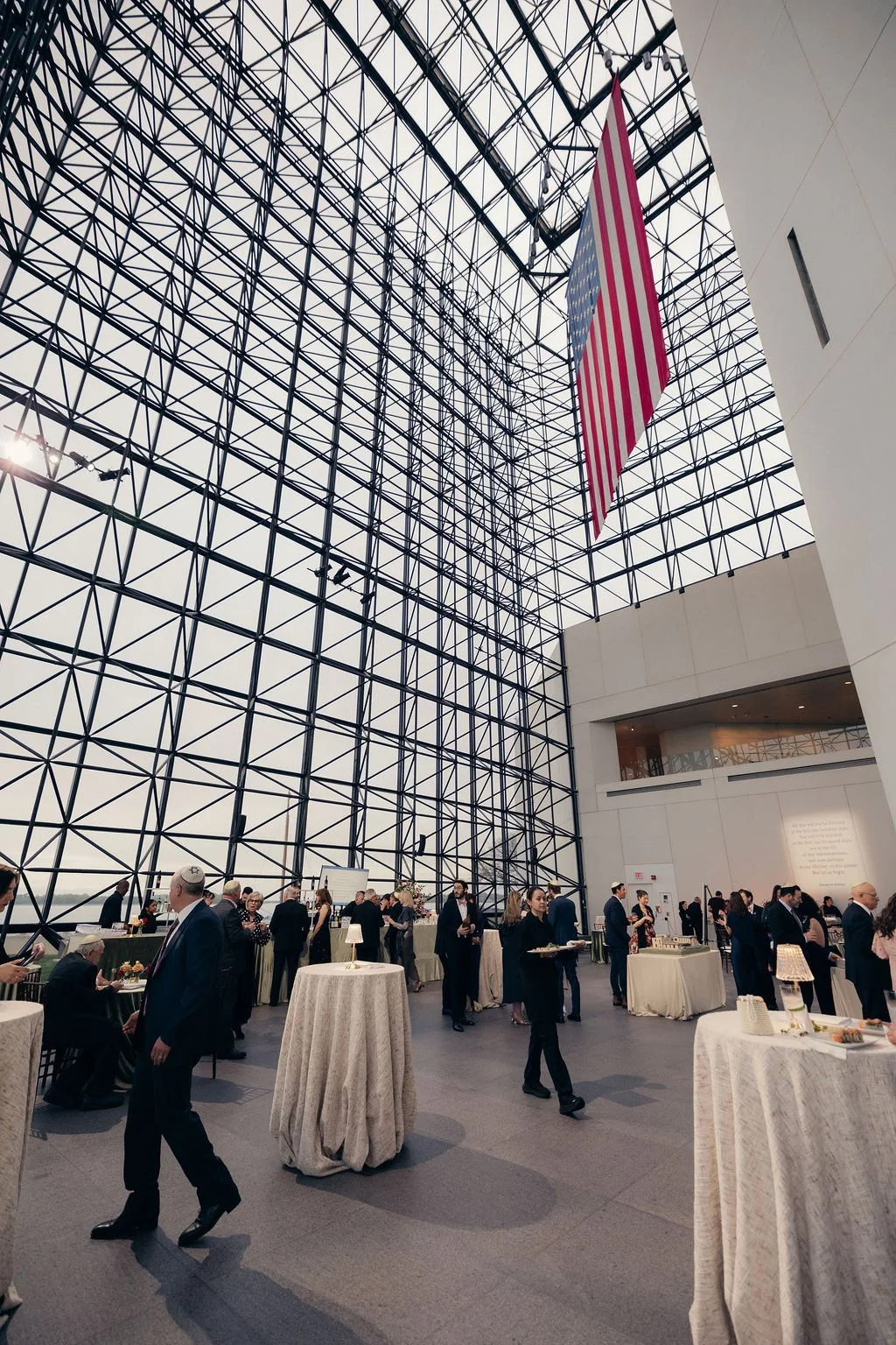 Cocktail tables fill a soaring glass atrium hung with a large American flag before the gala