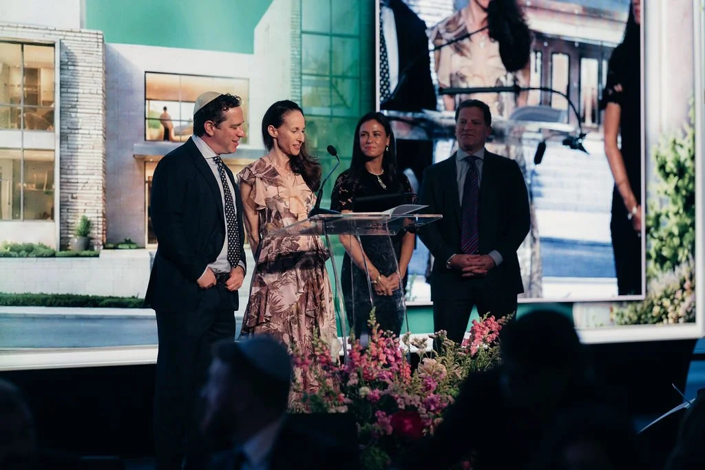 Honorees accept an award on stage in front of a house-themed backdrop at the Chabad Chestnut Hill gala