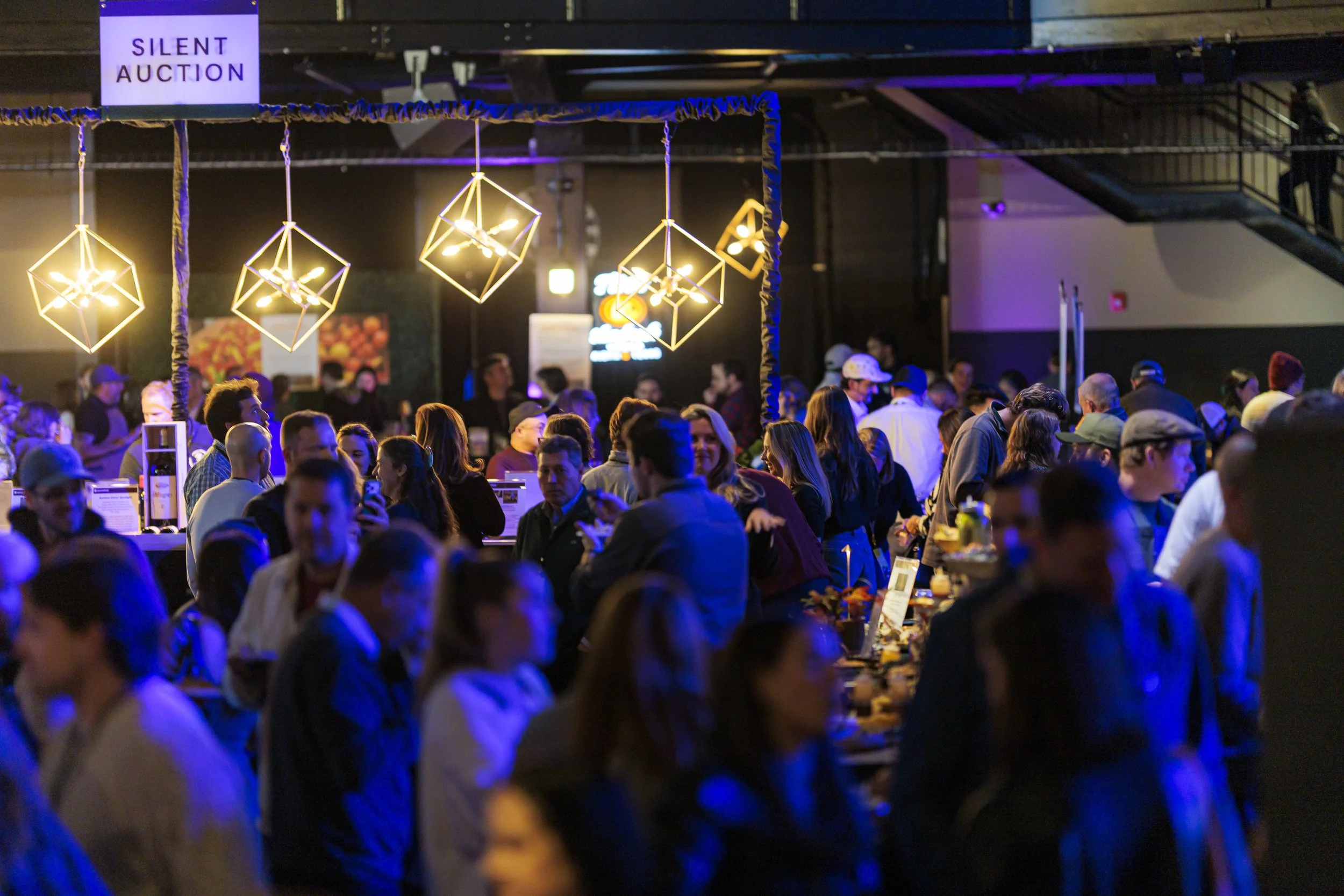 Guests browse the silent auction tables beneath hanging geometric lights at the Spoonfuls gala