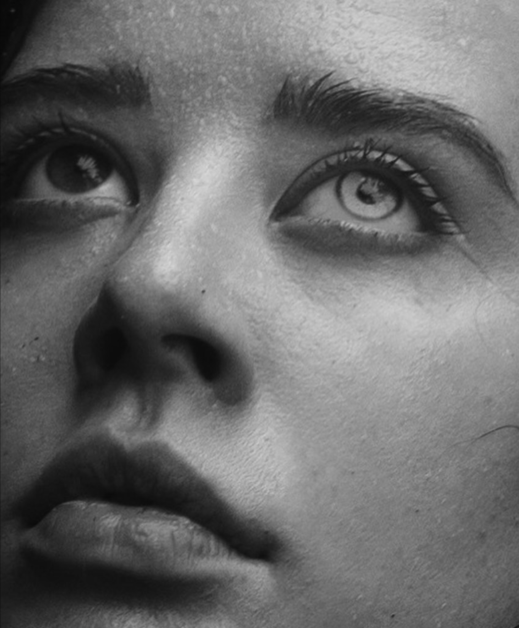 Close-up view of a person's eyes looking directly at the camera, with well-defined eyebrows and long eyelashes, captured in black and white.