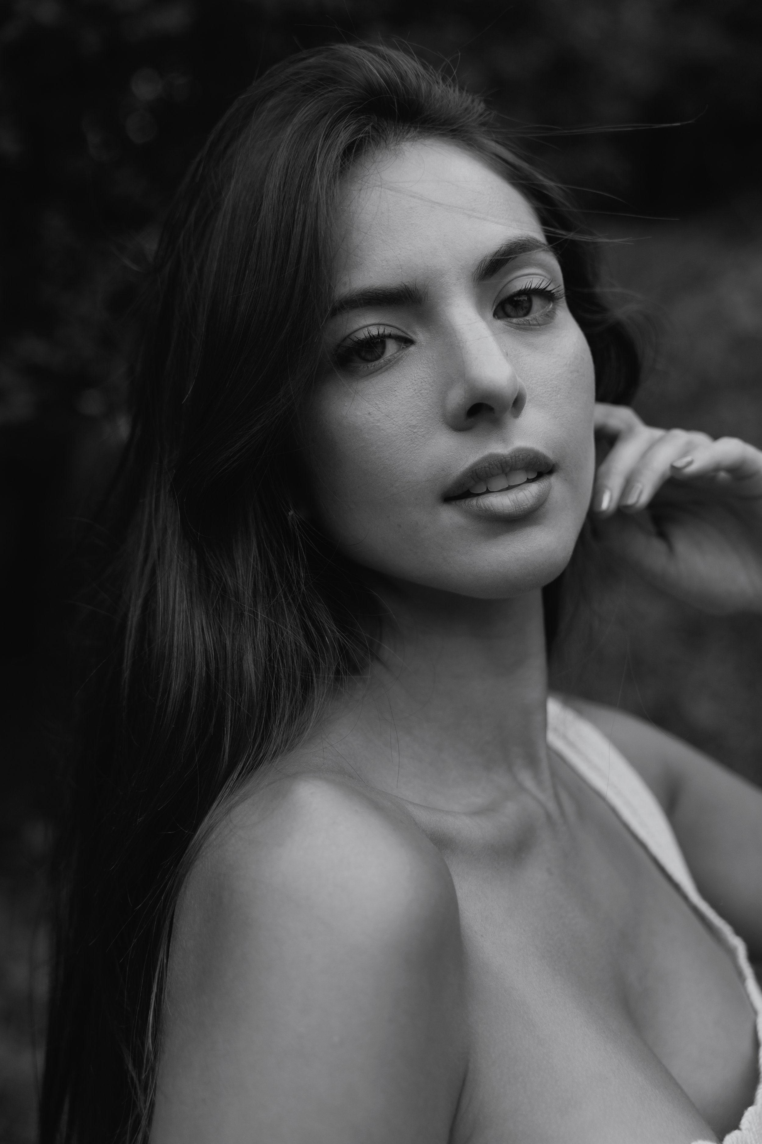 Close-up of a woman with long hair looking at the camera in black and white, with a blurred background.