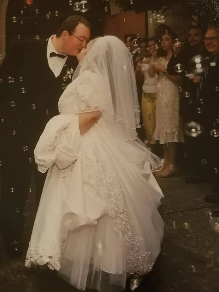A bride and groom share their first dance at a wedding reception, surrounded by guests, with bubbles floating around.