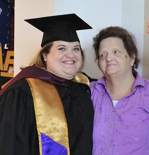 Young woman in graduation cap and gown smiling next to an older woman.