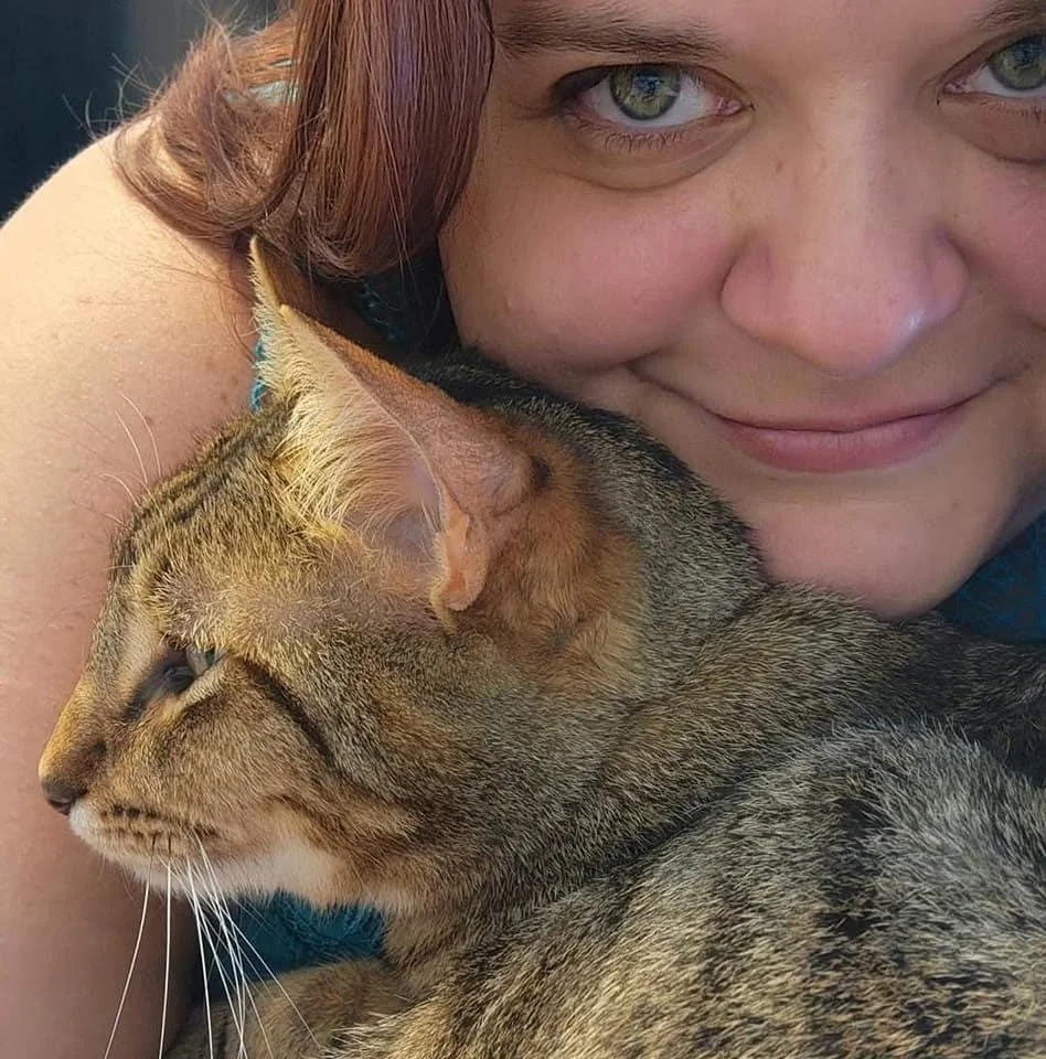 A woman with red hair smiling and cuddling a tabby cat.