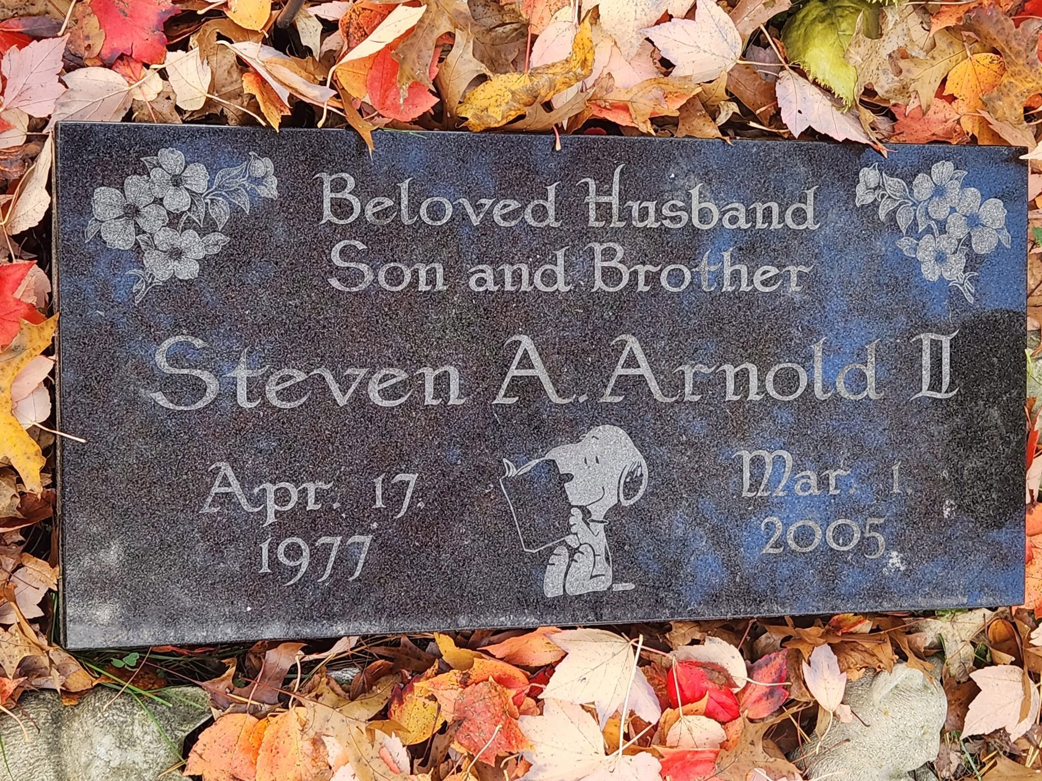 Gravestone with engraved text that reads: Beloved Husband, Son and Brother, Steven A. Arnold, April 17, 1977, March 1, 2005, surrounded by fallen autumn leaves.