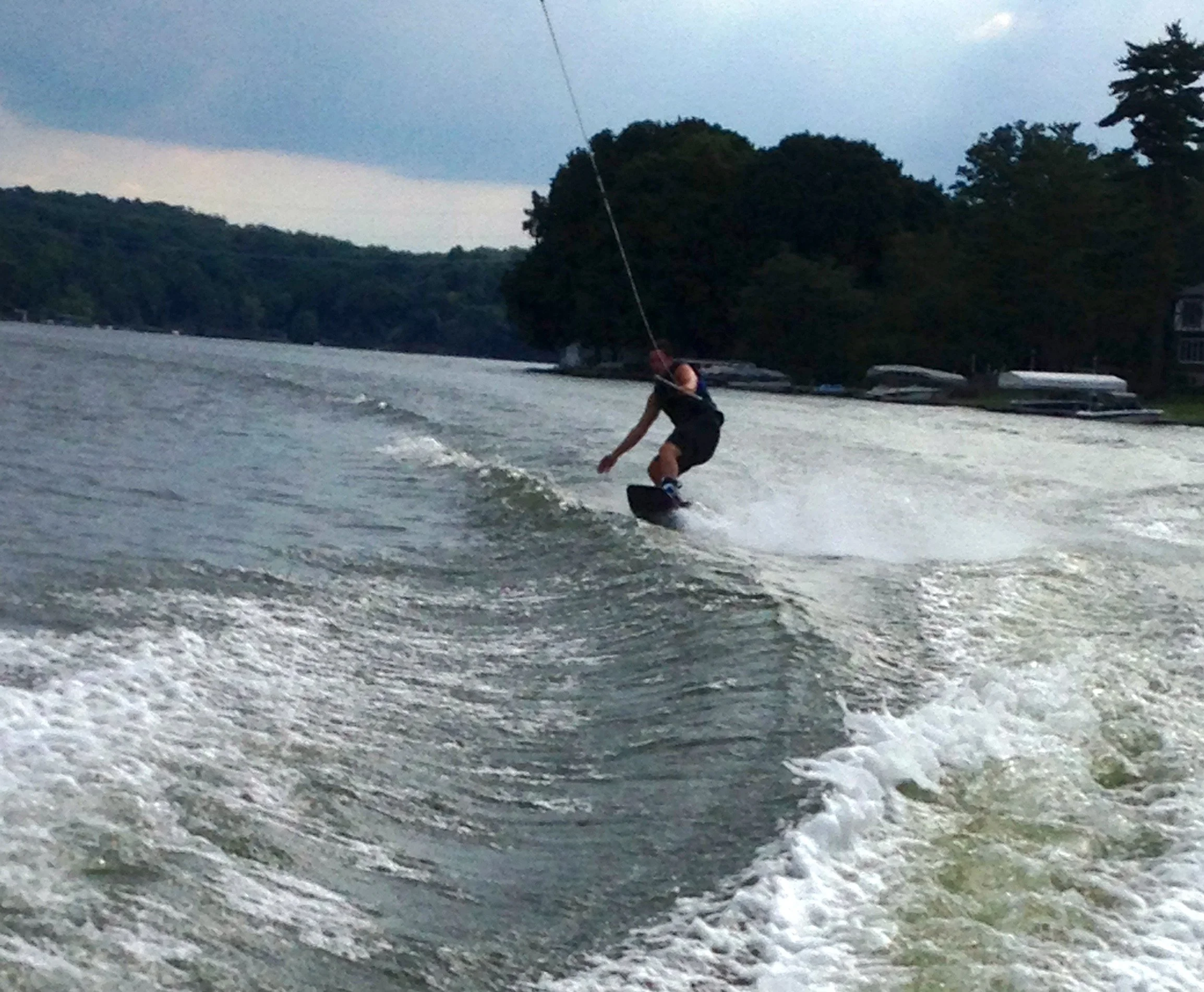 Person wakeboarding on a lake during evening with trees in background.