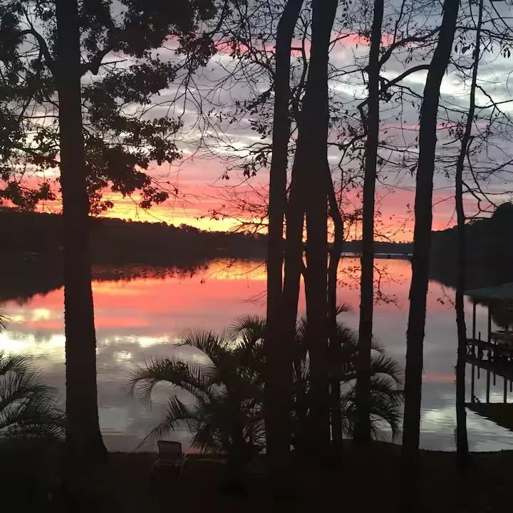 Sunset over a lake with reflections of colorful sky, silhouetted trees and a small dock on the right.